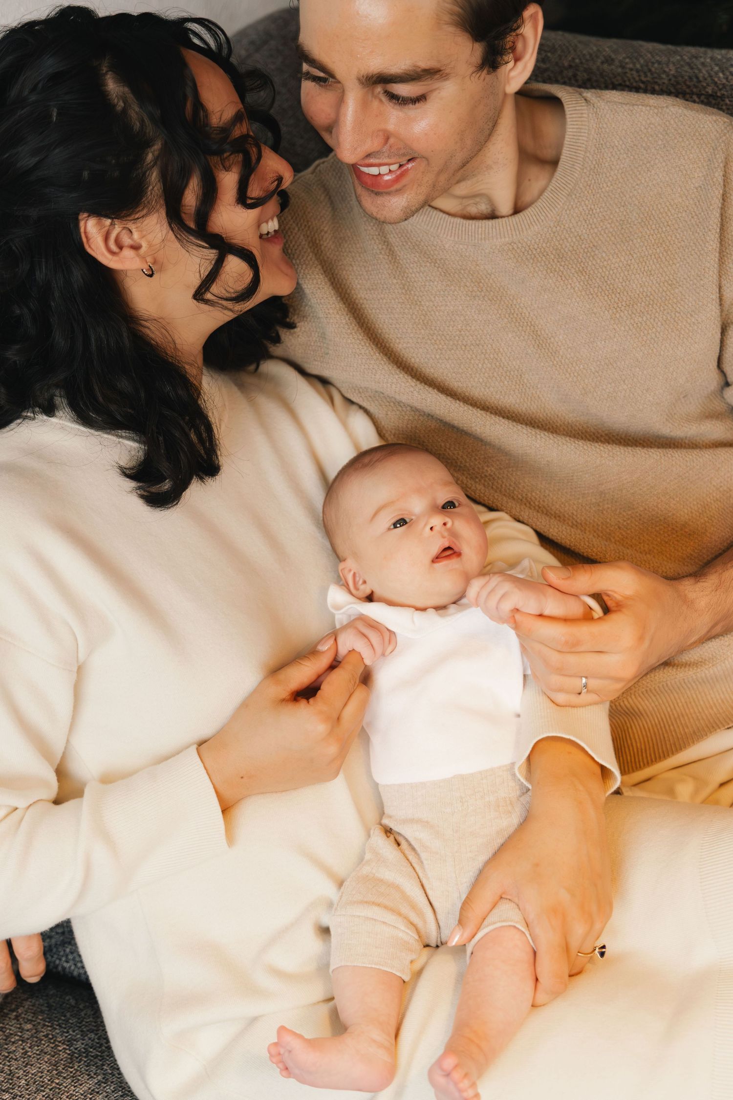 Parents smiling at each other while holding their newborn during a newborn photoshoot in Switzerland.
