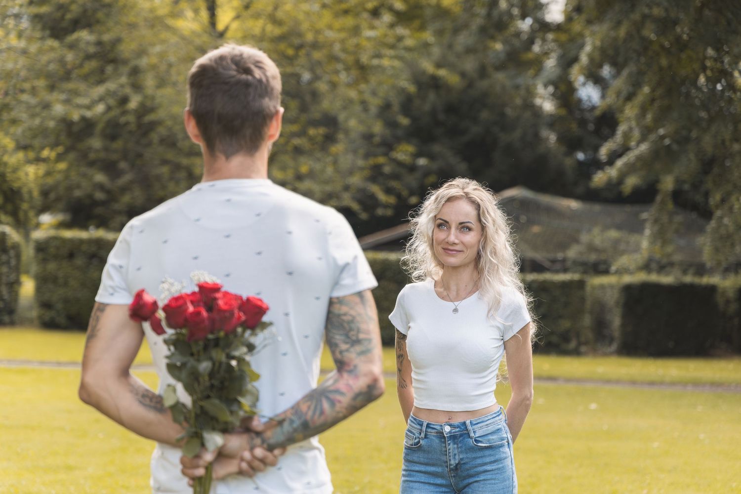 Man hiding a bouquet of flowers behind his back while his partner looks into his eyes during a romantic couples photoshoot.