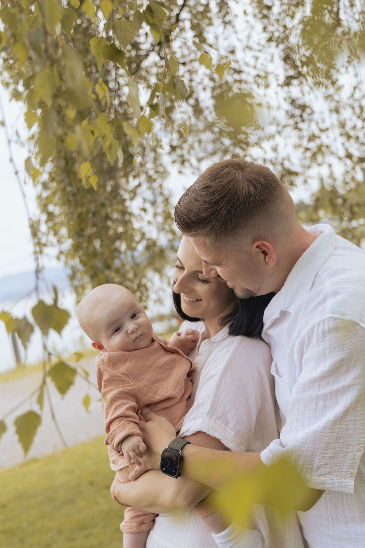 Parents holding their baby between trees during an outdoor family photoshoot in Switzerland.