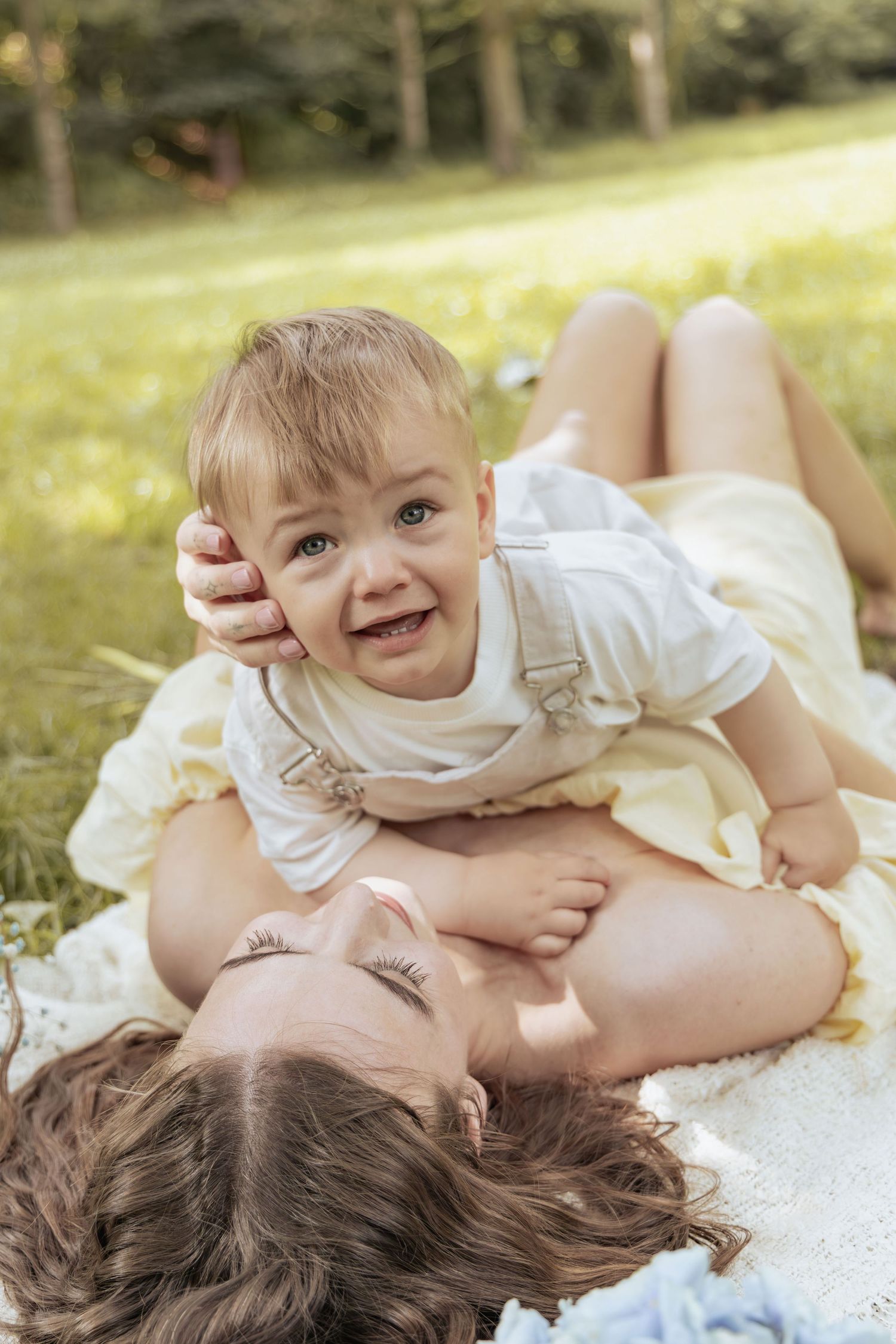 Mother and son laughing together on a blanket during a joyful family photoshoot in the park.