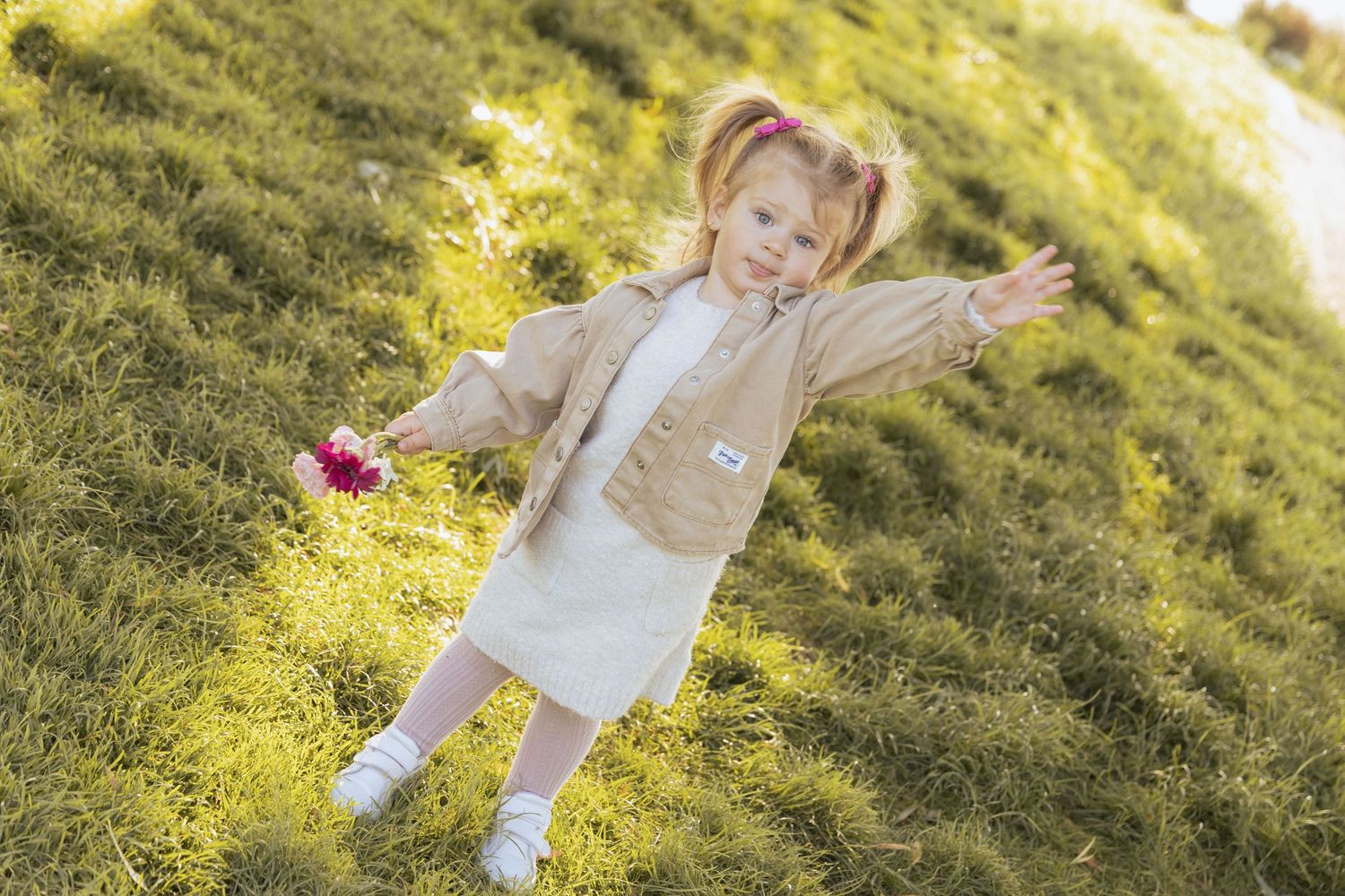 Little girl waving with soft sunlight behind her during a natural light outdoor photoshoot.