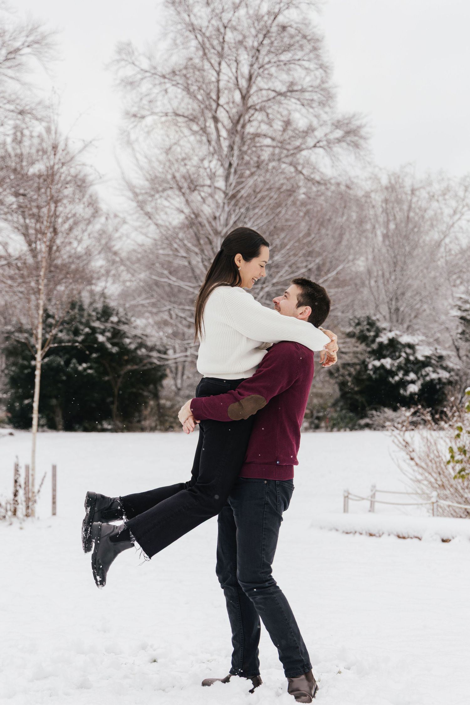 Man lifting his partner in the air while enjoying a snowy couples photoshoot in a Swiss park.