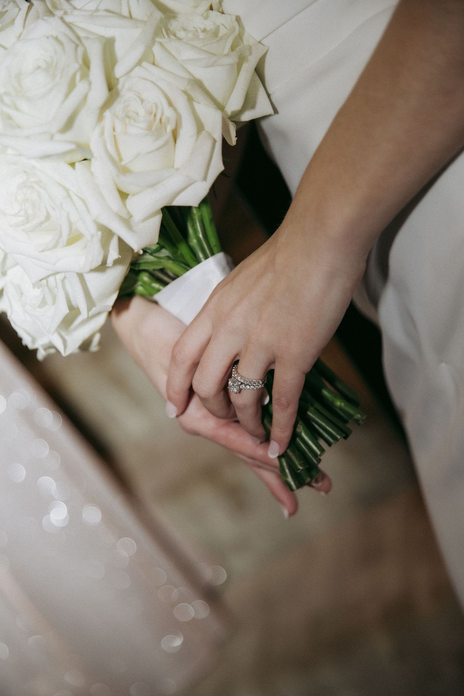 Close-up of hands holding a white rose bouquet with a sparkling engagement ring.