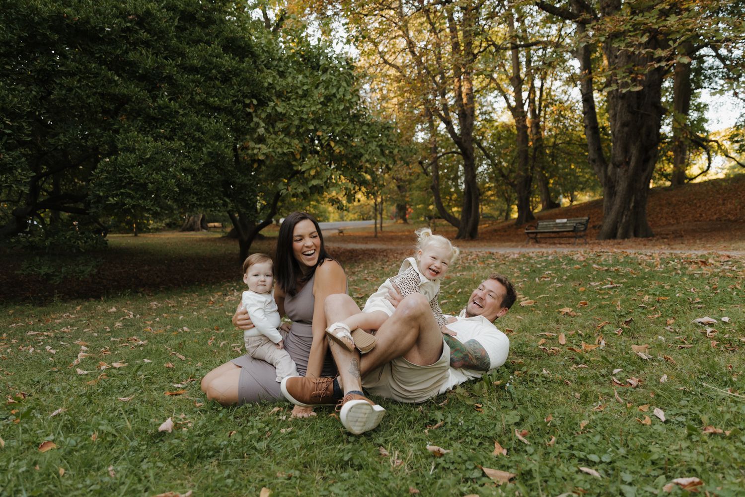 People enjoying a playful moment together while lying on autumn leaves in a park setting.