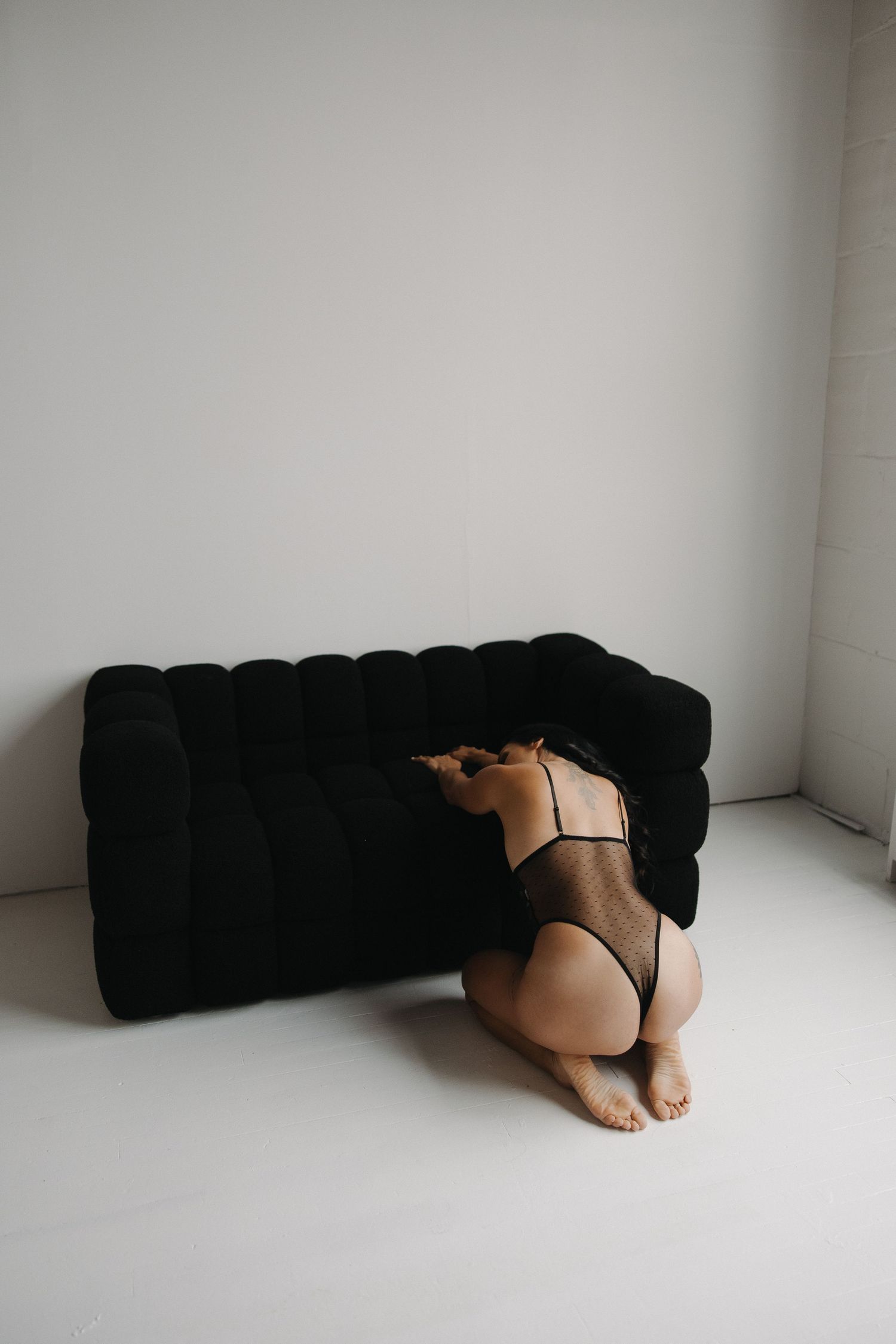 A minimalist series of five black and white photographs showing a person curled up against a white wall.
