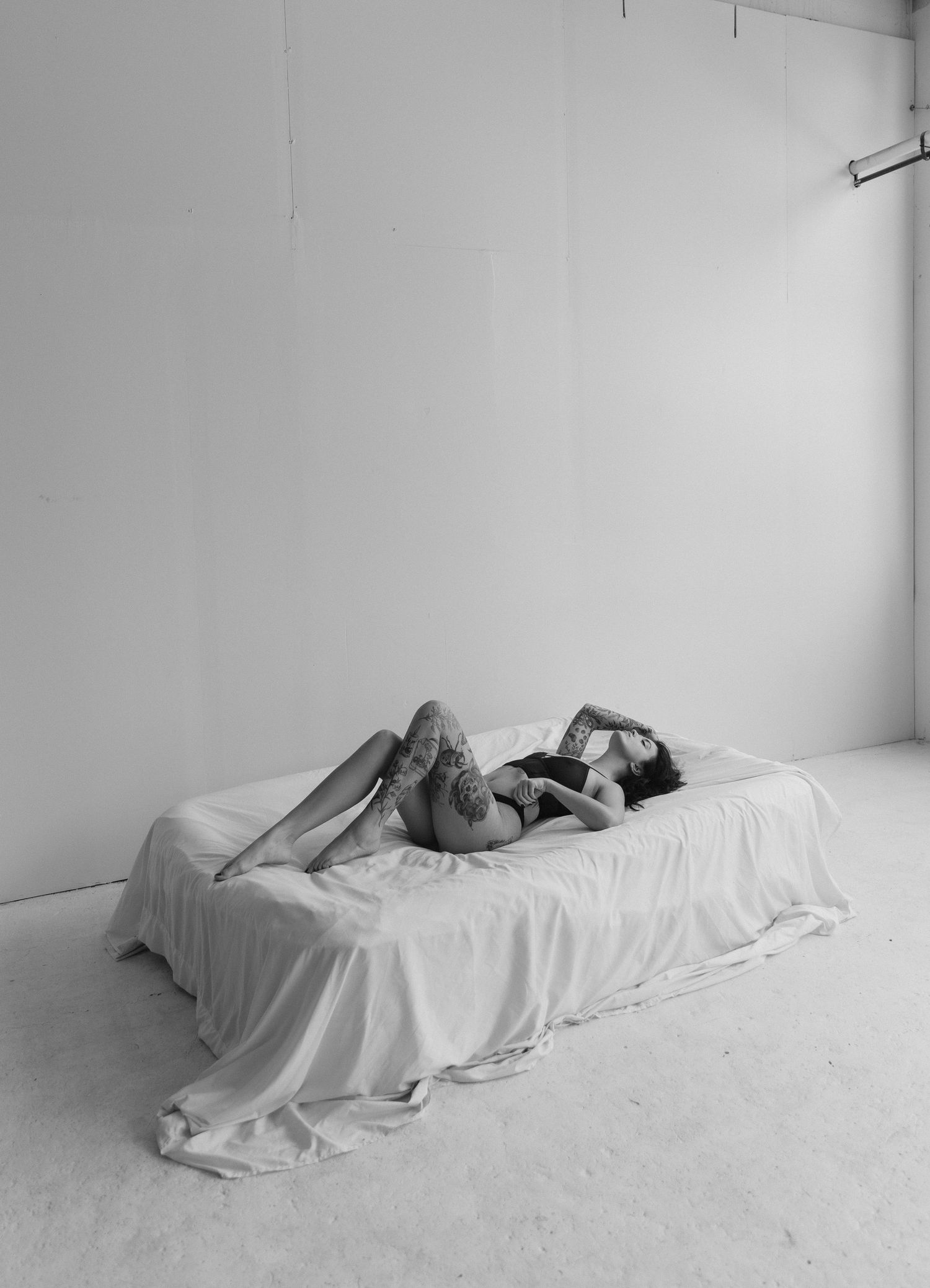 A figure lies motionless under white sheets in a minimalist black and white art installation series.