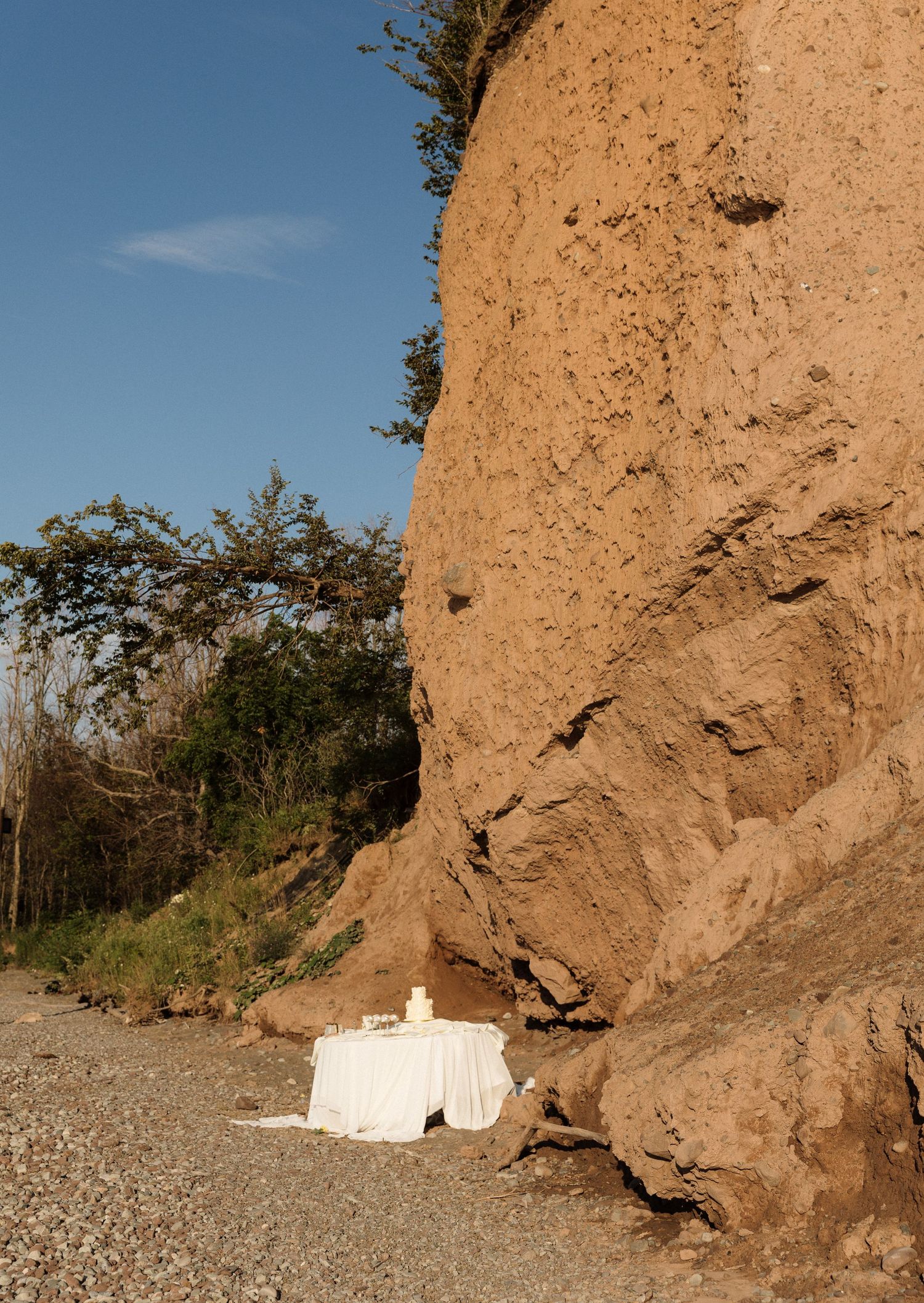 Panoramic sequence of eroded clay cliffs along a rocky beach shoreline under blue sky.