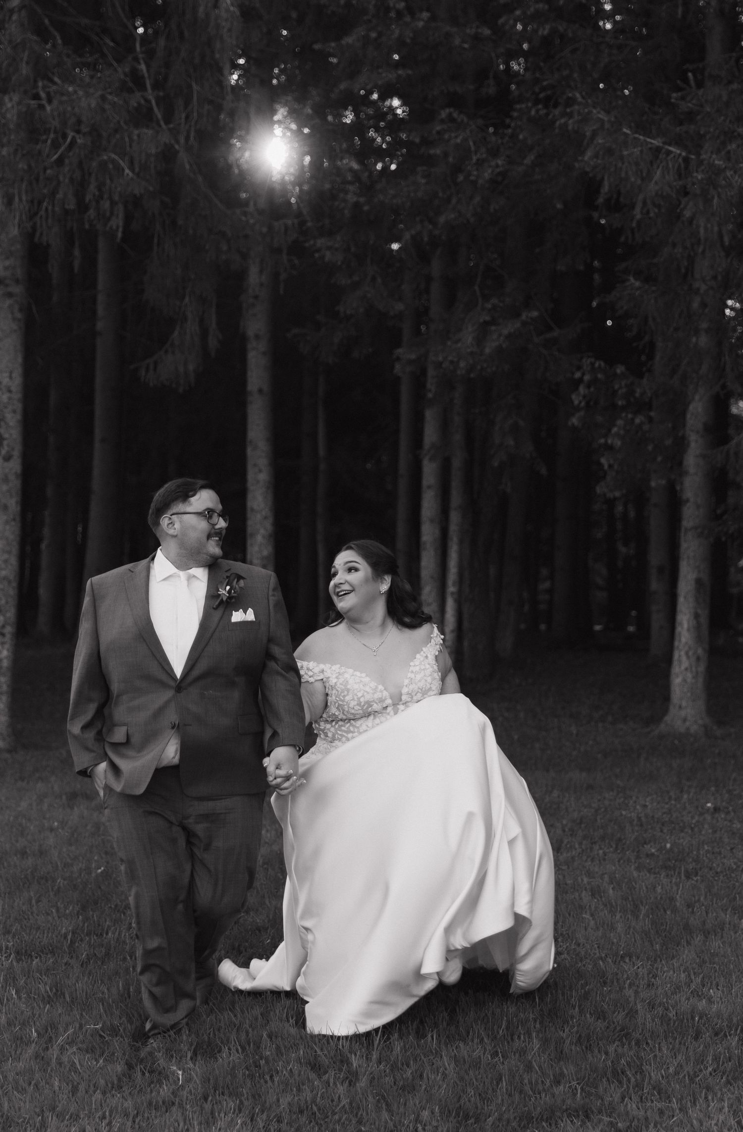 Black and white photo of newlyweds dancing together in a wooded evening setting.