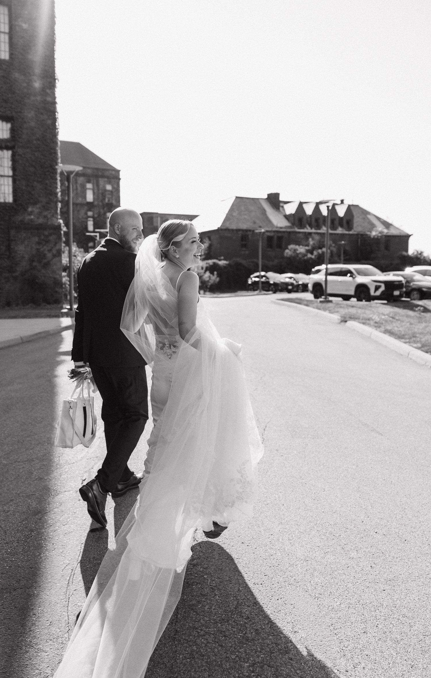 Black and white photo of a bride and groom walking together outdoors on their wedding day.