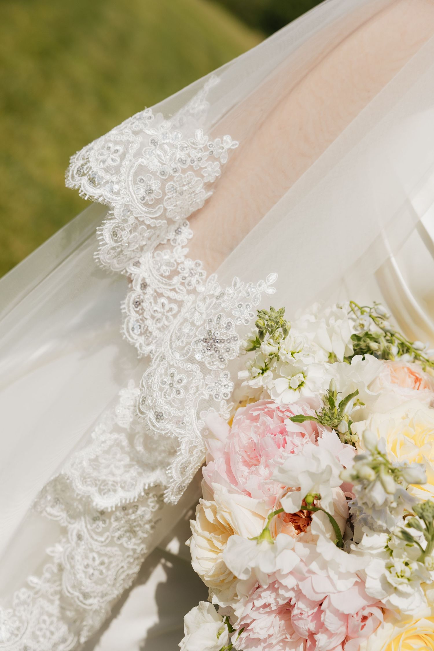Elegant bridal veil with intricate lace trim beside a soft pink and white wedding bouquet of peonies and roses.