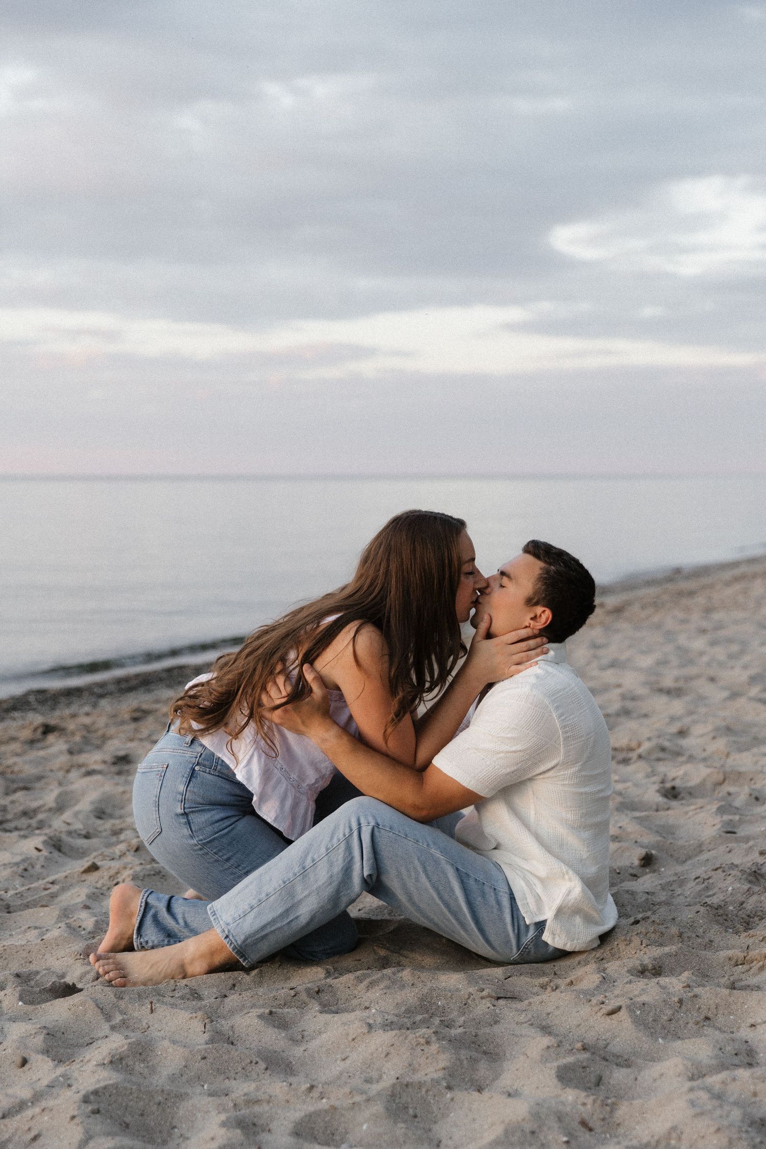 Romantic couple sharing an intimate moment while sitting on a sandy beach at sunset with ocean in background.