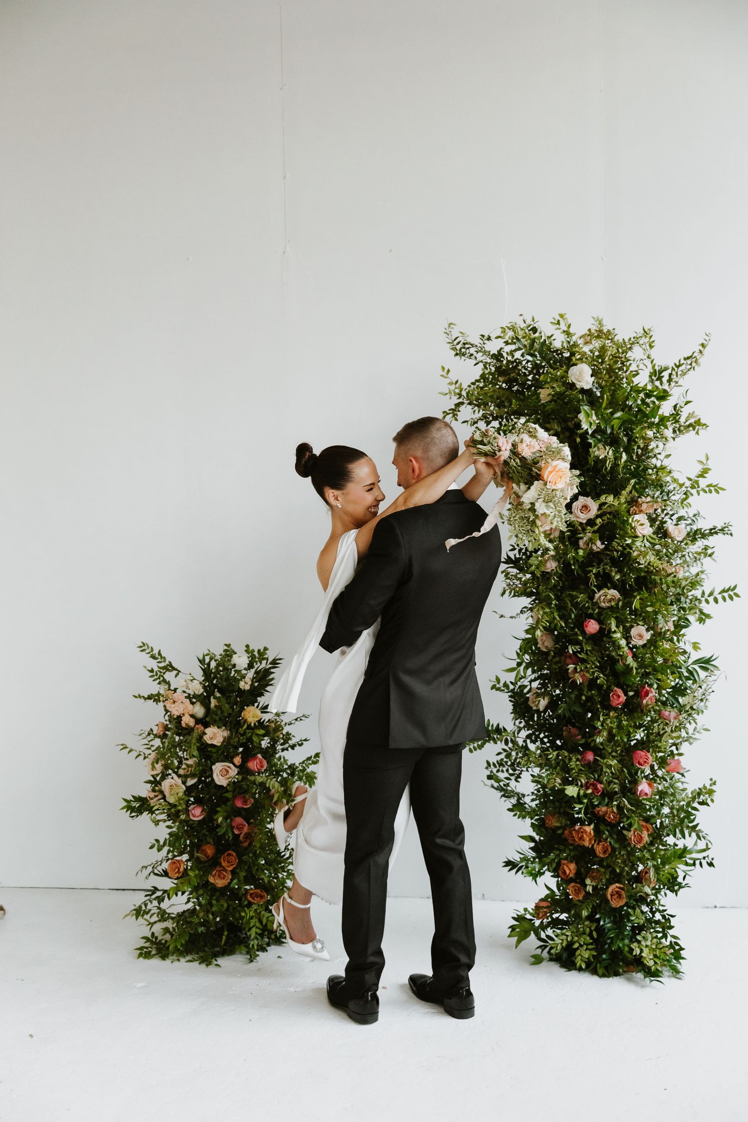A romantic dance sequence between two people in formal attire against a backdrop of floral arrangements with roses and greenery.