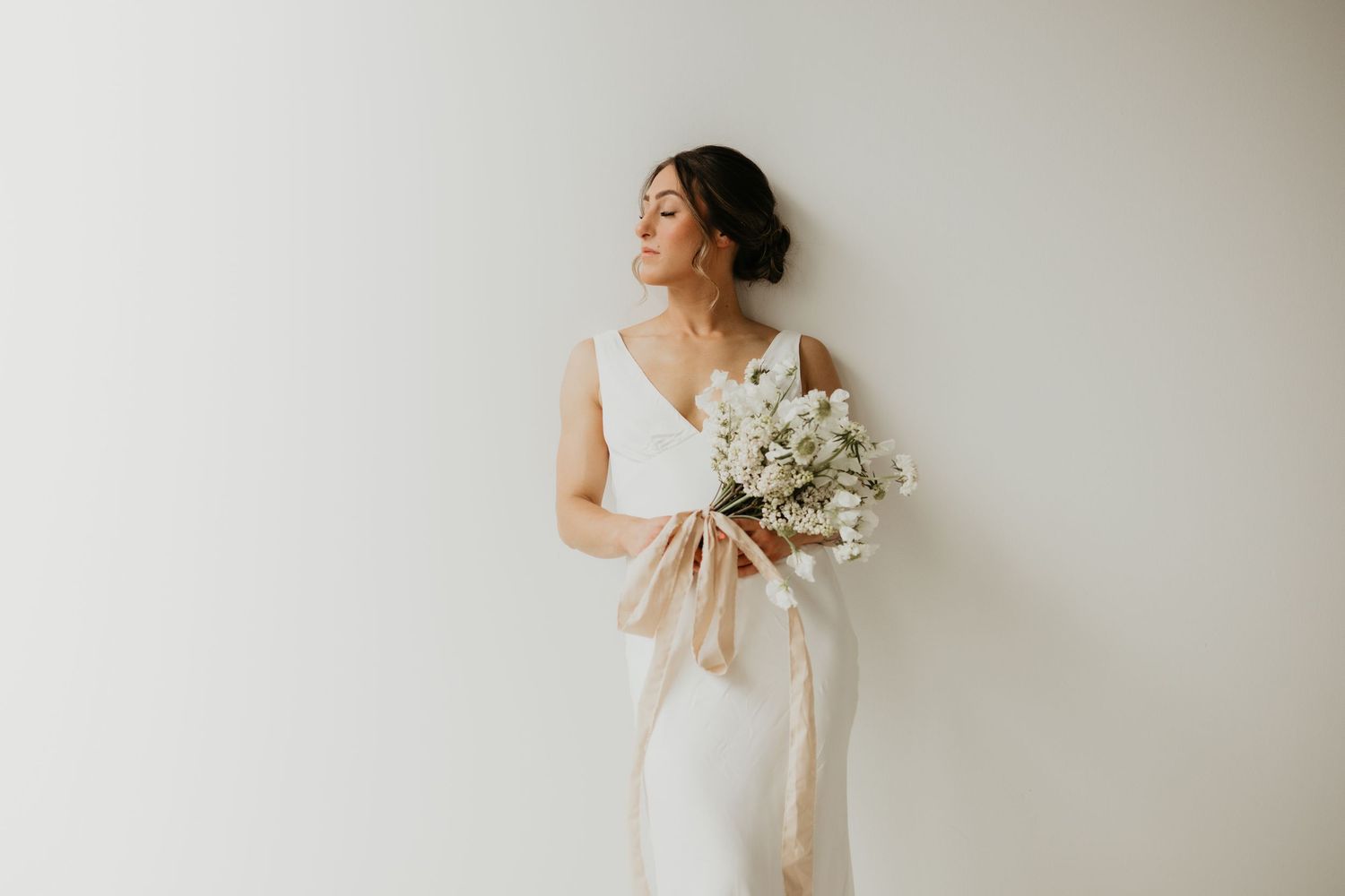 Minimalist bridal portrait series against white backdrop with delicate floral bouquet.