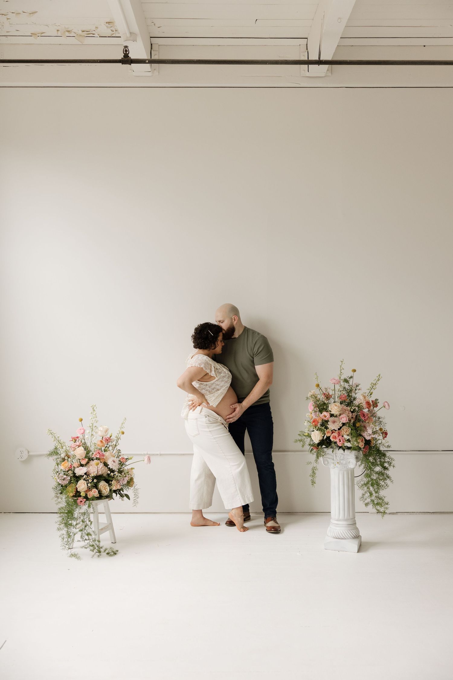 A minimalist white studio space with floral arrangements showing a progression of someone styling flowers on a pedestal.
