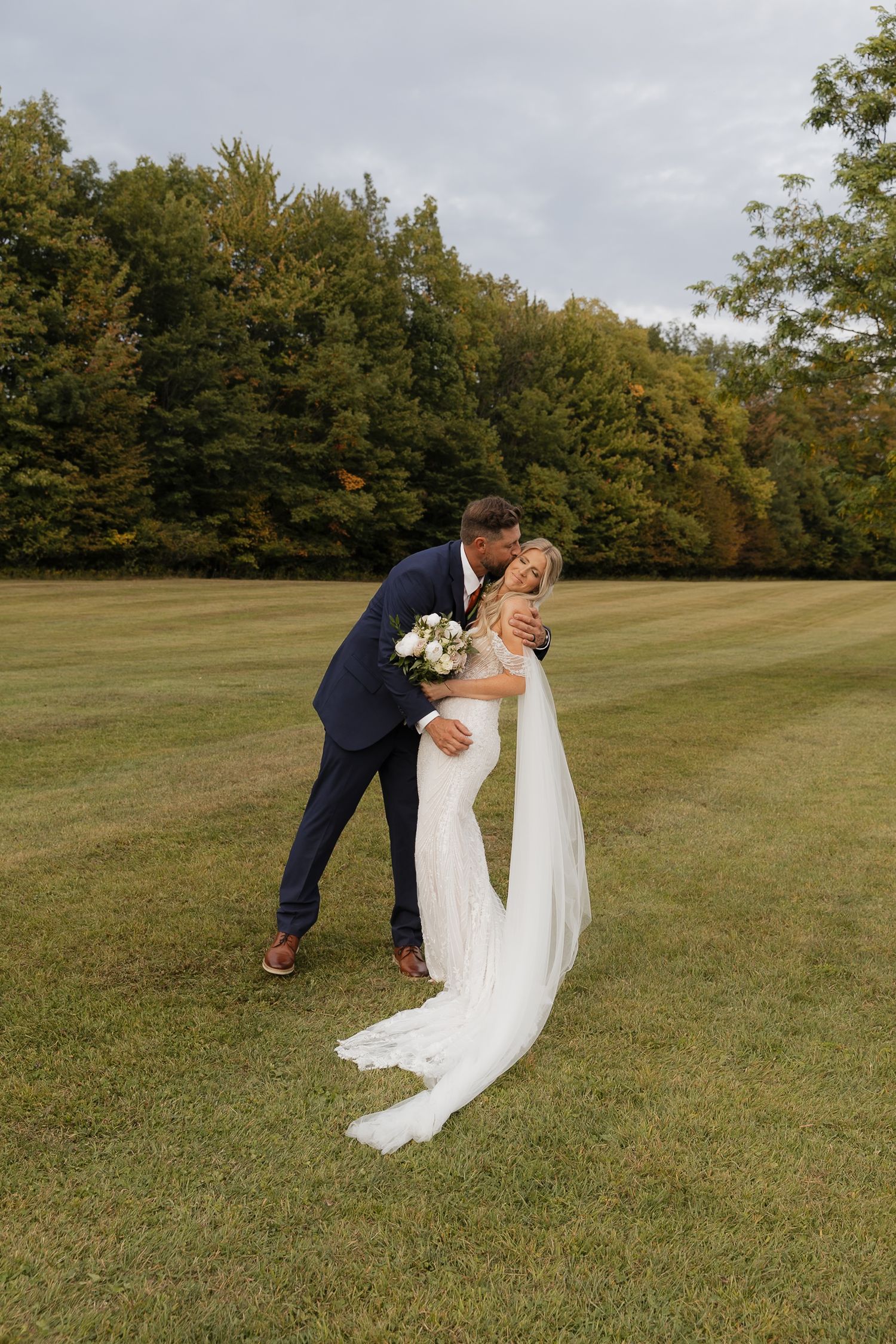 A couple in wedding attire playfully poses in a series of photos on a grassy hillside during an autumn day.