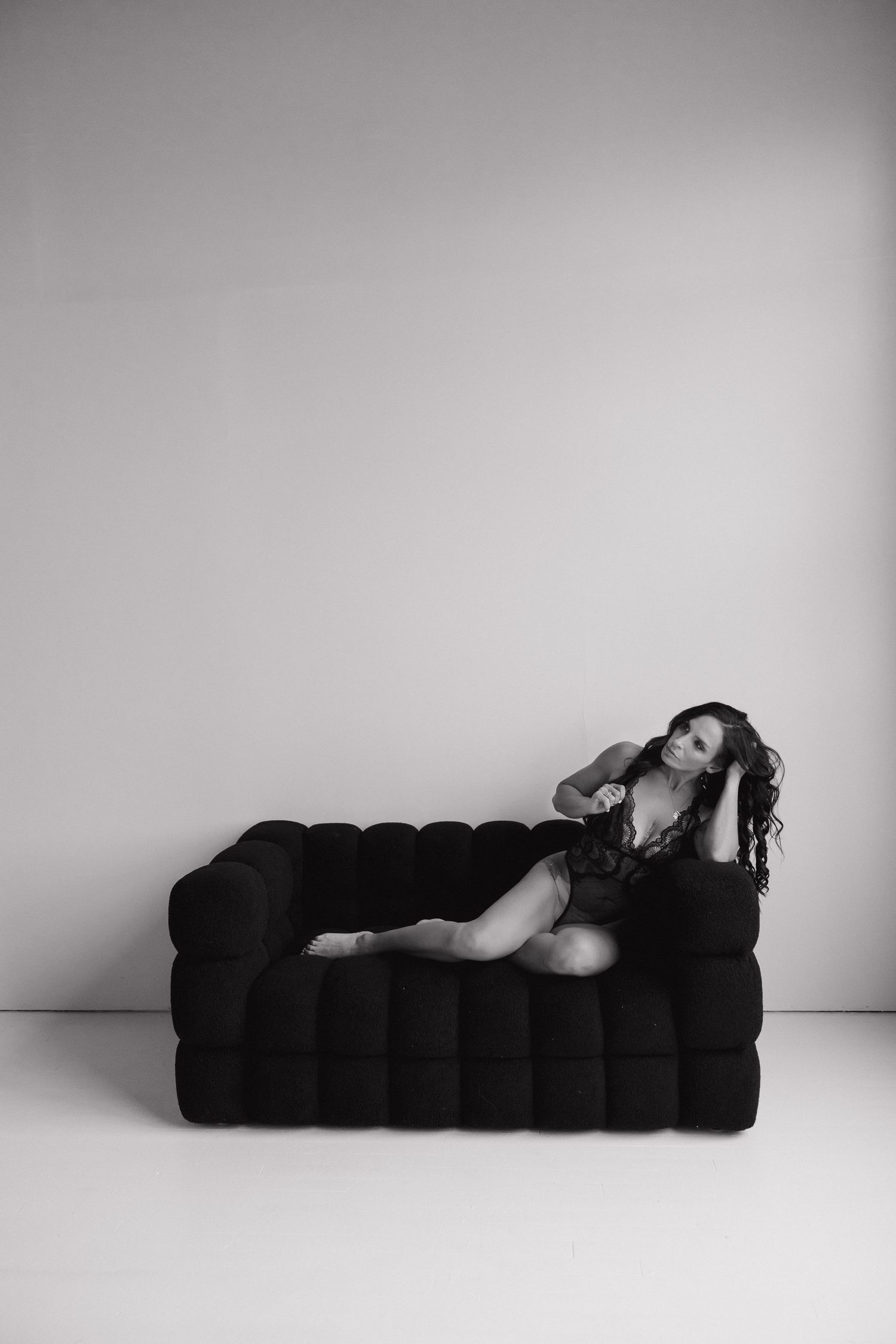 Dramatic black and white poses on a tufted black chaise in a studio setting.