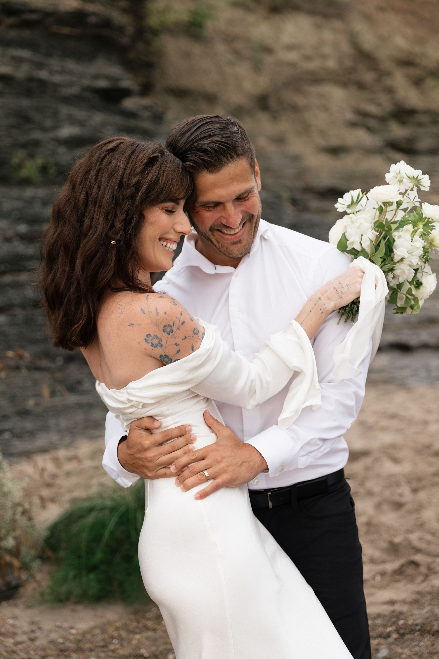 A romantic couple in formal attire embraces on a rocky beach setting in a series of candid photos.