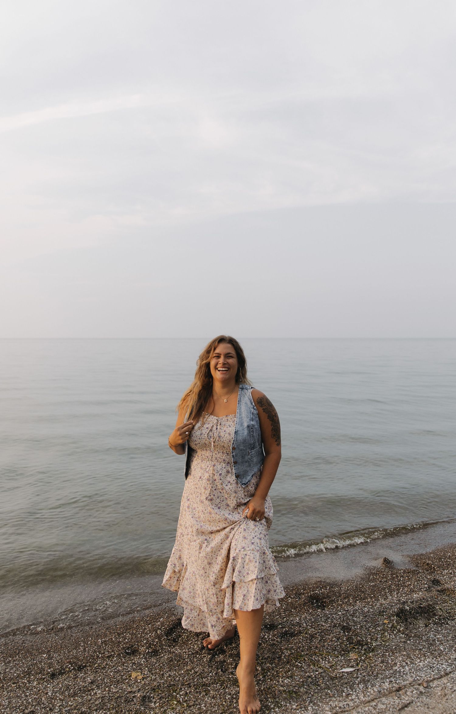 Woman in floral dress walking along a misty beach shoreline.