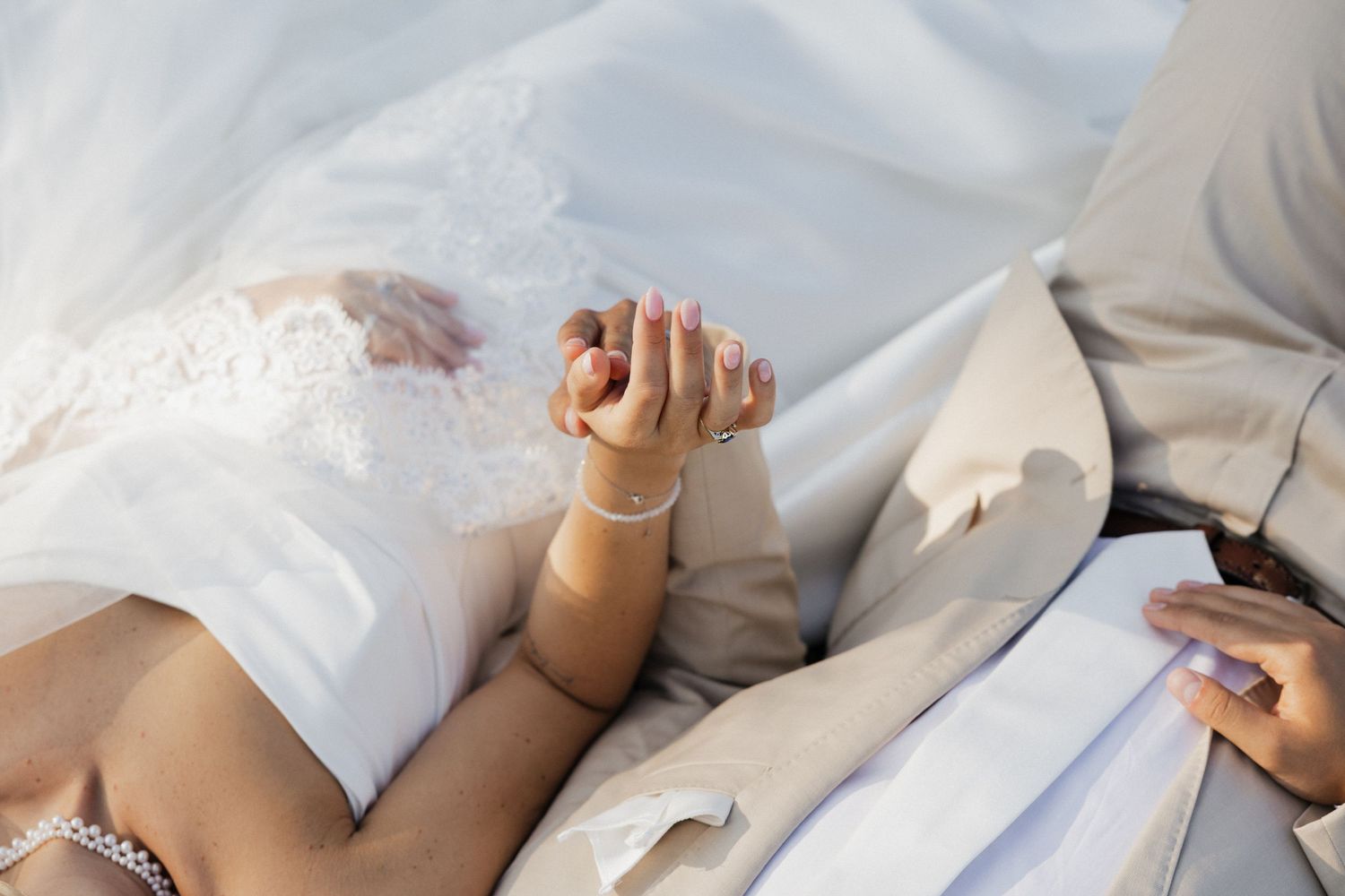 Bride and groom holding hands tenderly, wedding dress visible, close-up romantic detail shot.