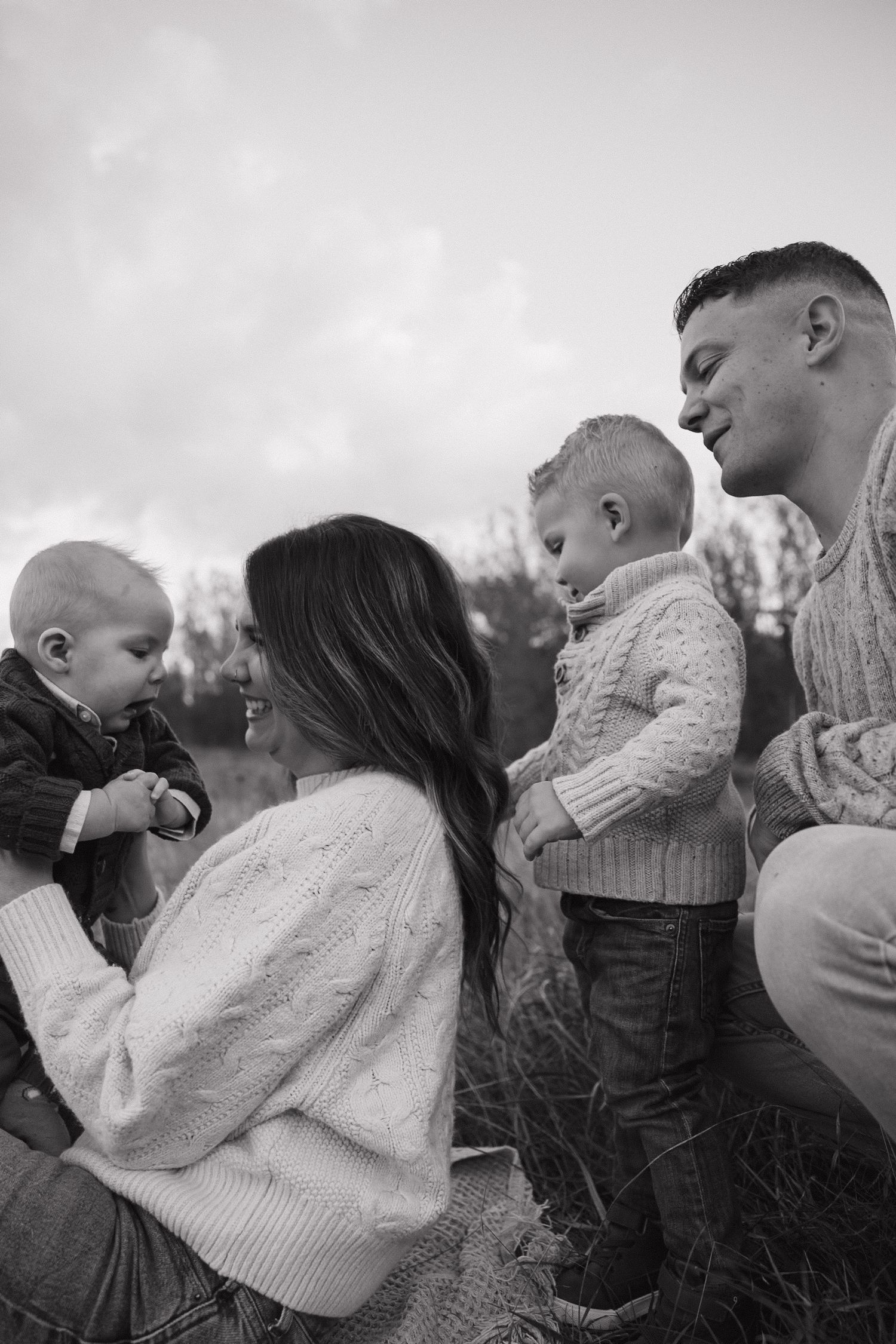 Black and white family photo of parents with two young toddlers outdoors in a field during autumn.