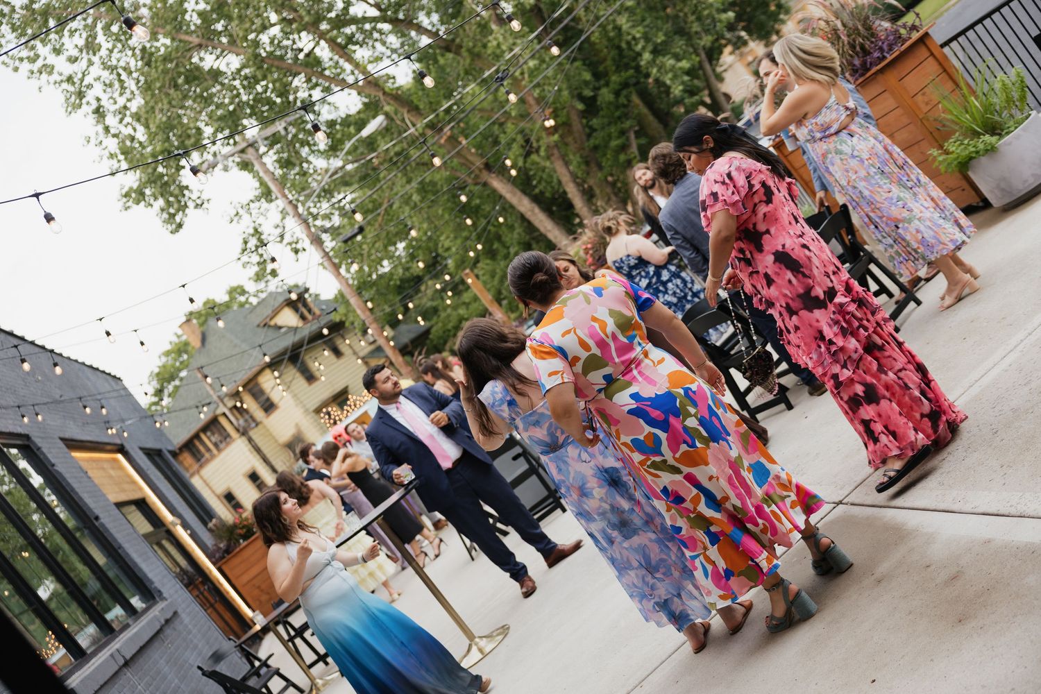 Women in colorful floral dresses gathered outdoors at a festive garden party event with string lights.