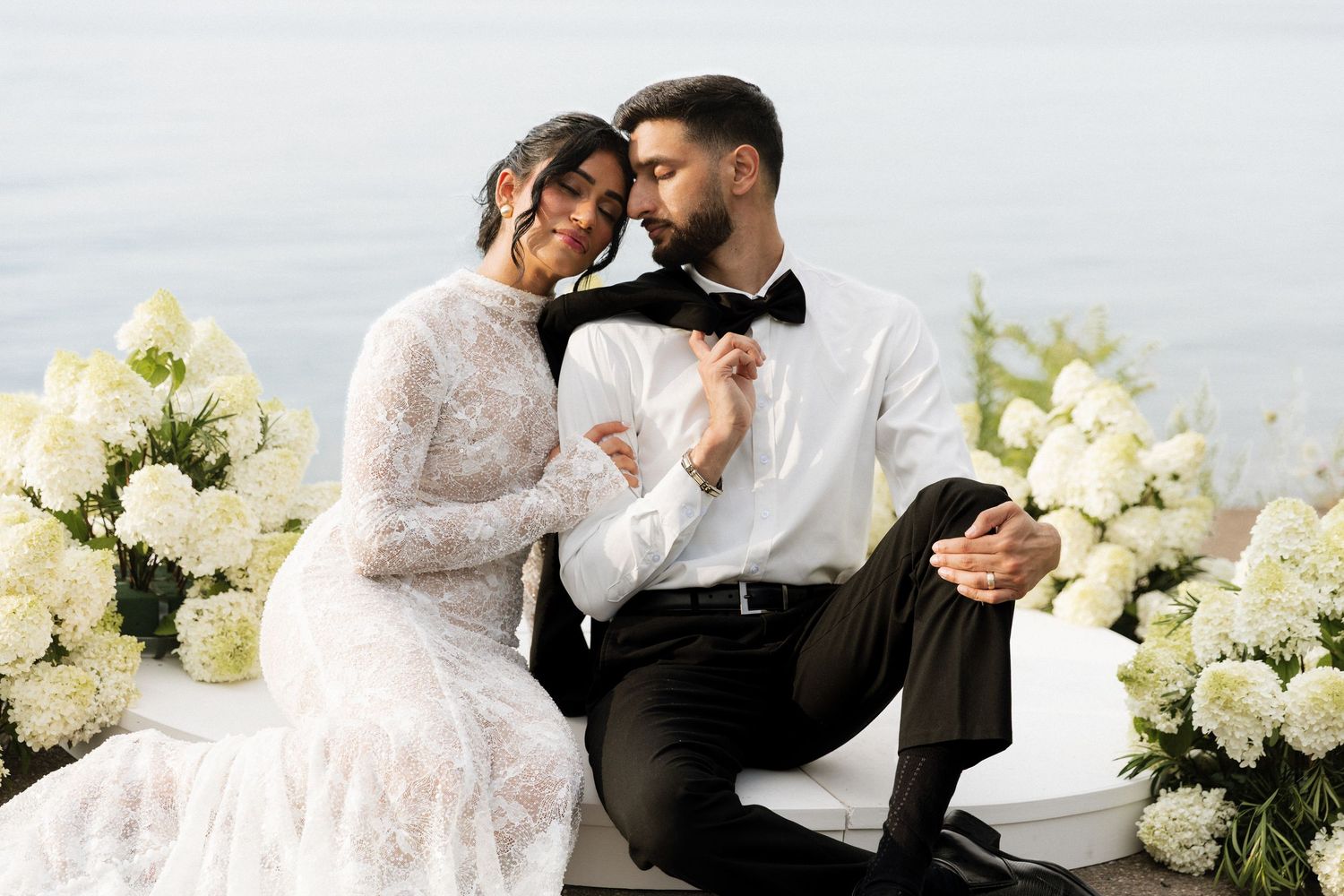 A romantic wedding couple shares intimate moments together surrounded by white floral arrangements.
