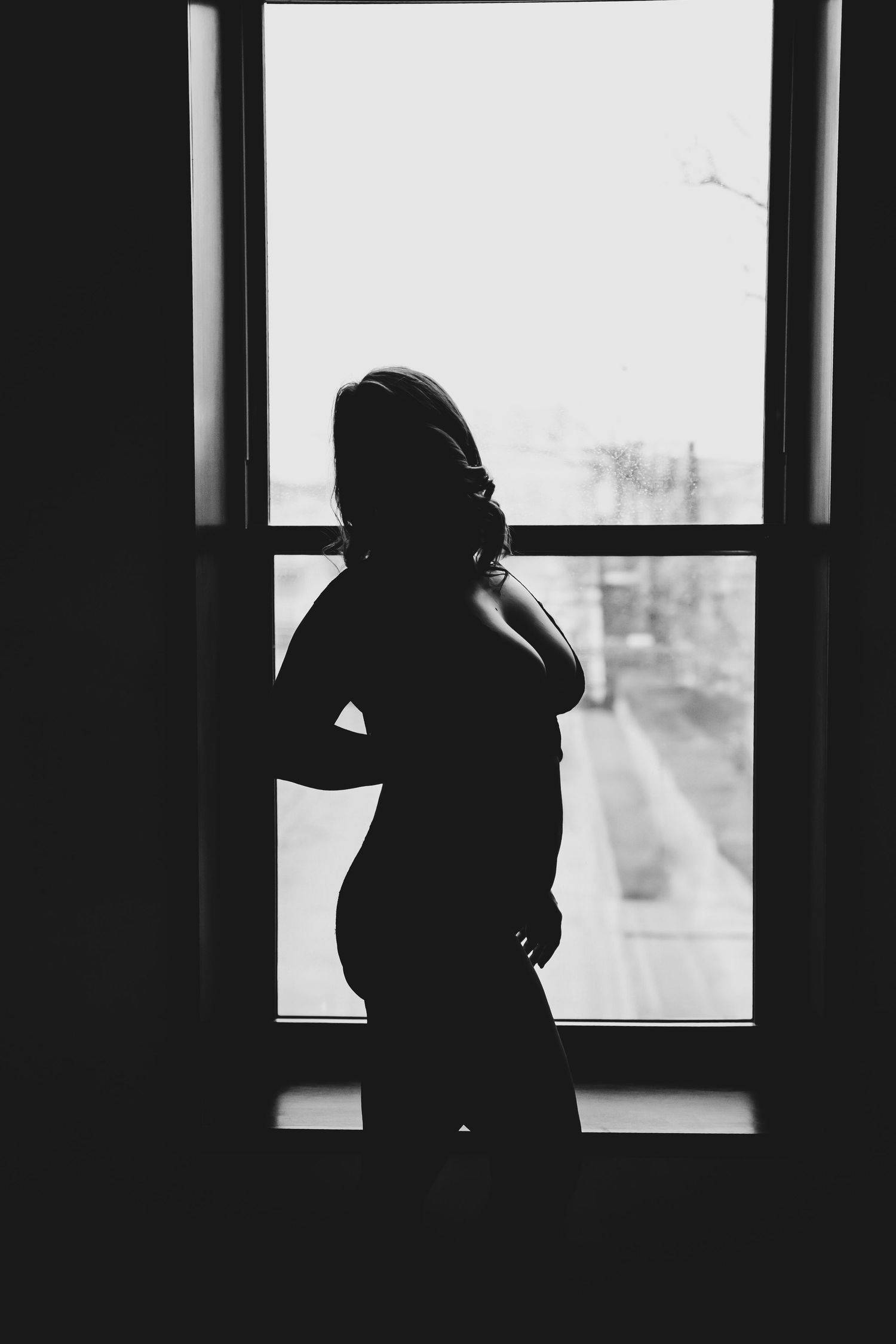 Black and white silhouette of a pregnant woman standing by a window.