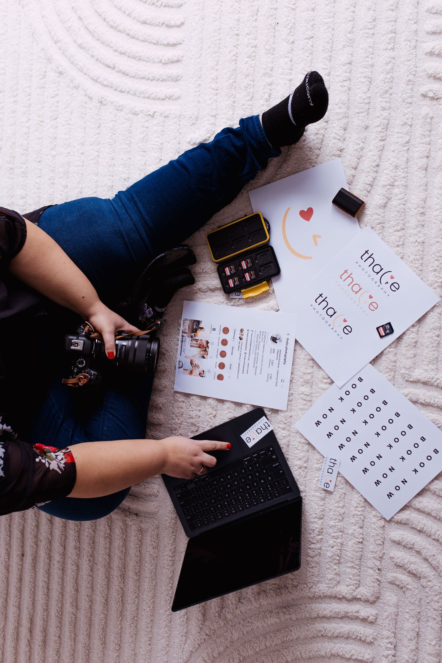 Overhead view of photographer sitting with camera, tablet, and branding documents on white carpet.