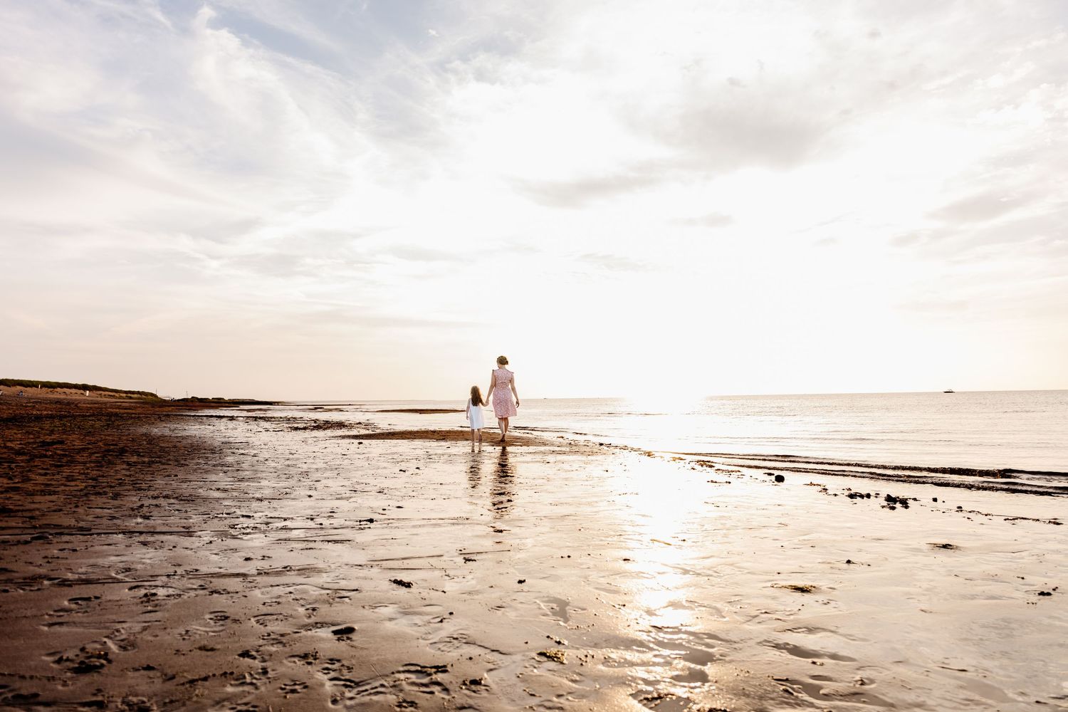 Couple walking hand in hand along a reflective beach at sunset.