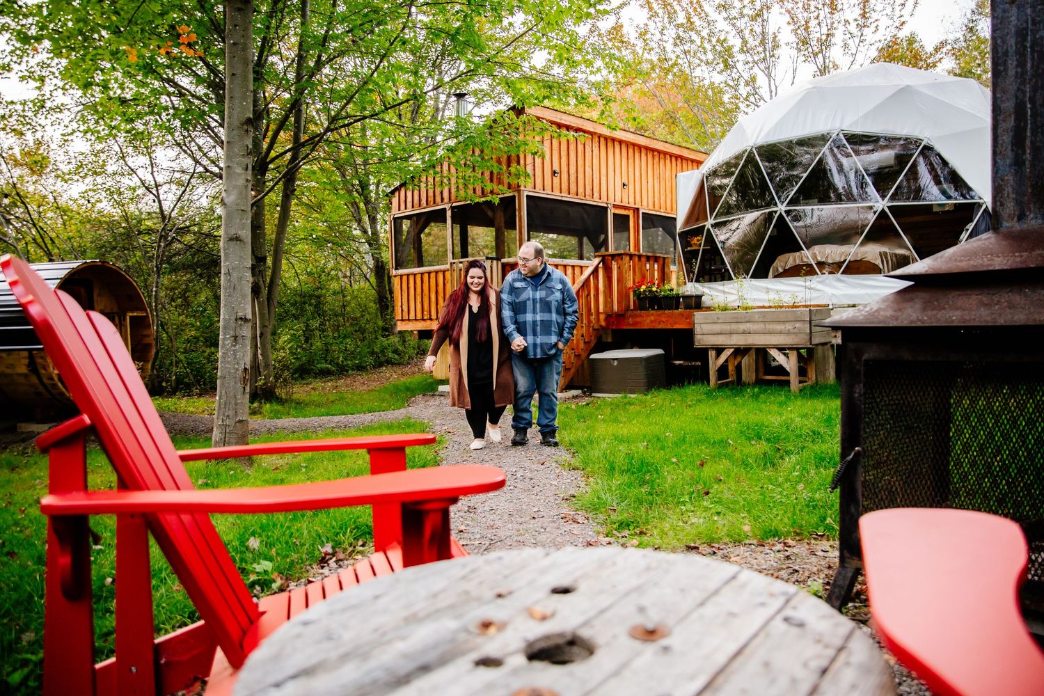 Couple walking through glamping site with geodesic dome and wooden treehouse in autumn.