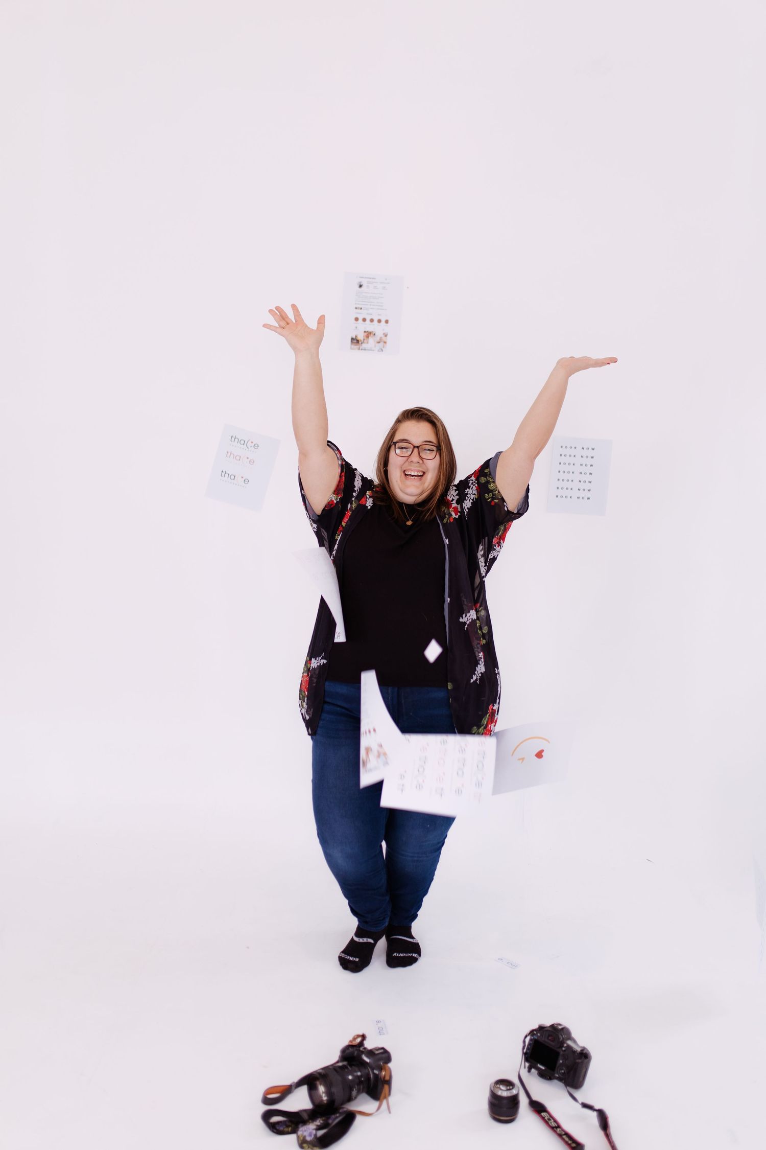 Thalie photography Excited female photographer tossing papers in air with cameras on floor in white photography studio.