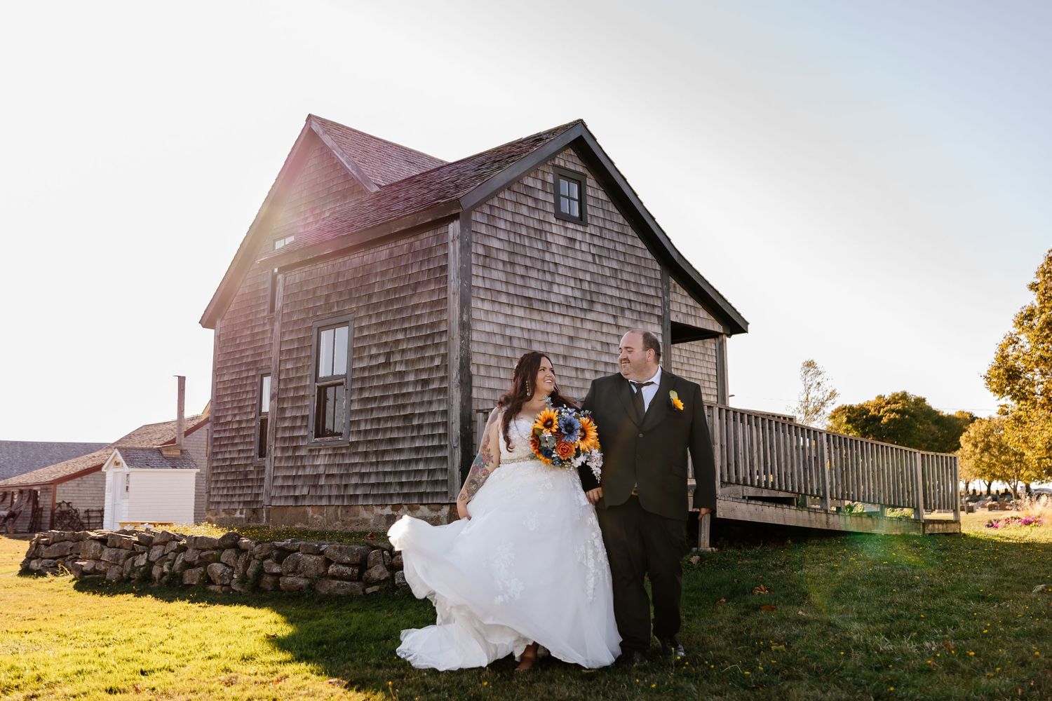 Bride and father walking together outside rustic wooden building on sunny wedding day. Grande-Digue