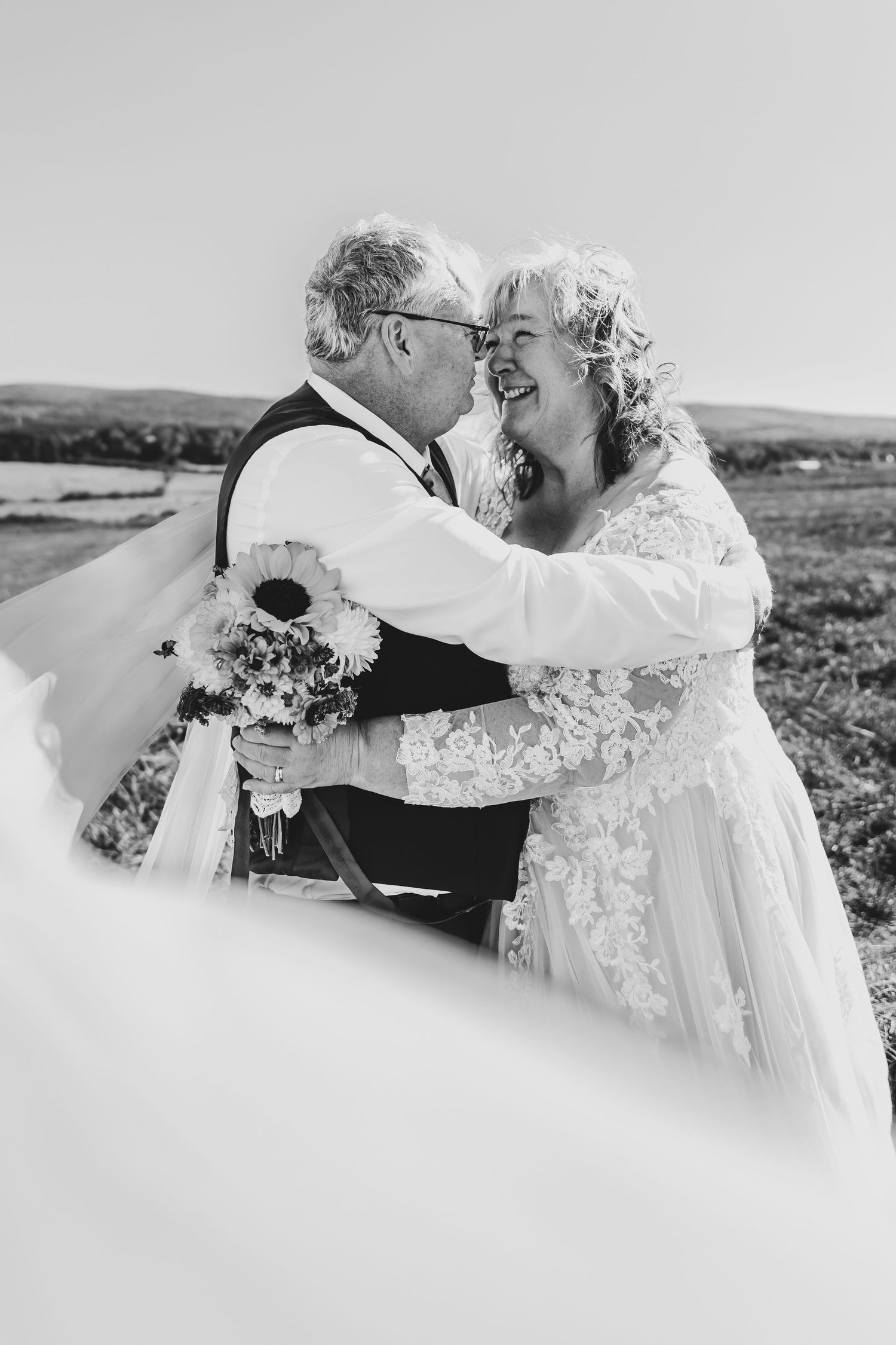 Older couple sharing a romantic kiss on their wedding day outdoors in a black and white photo.