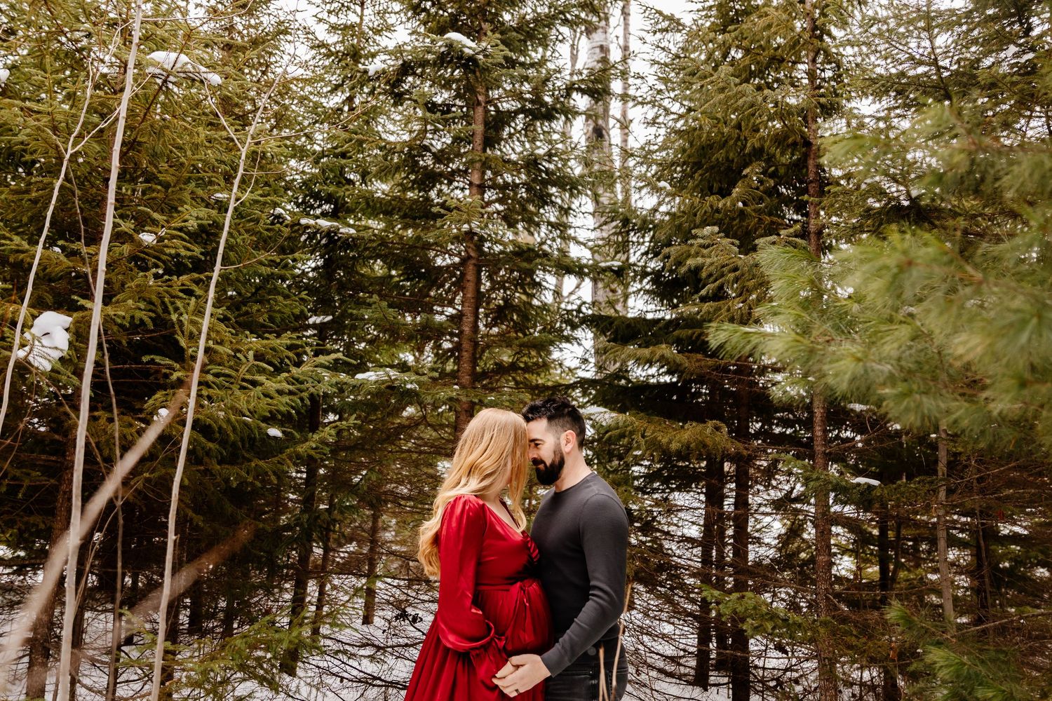 Romantic couple embracing in snowy pine forest, woman wearing red dress. Dieppe
