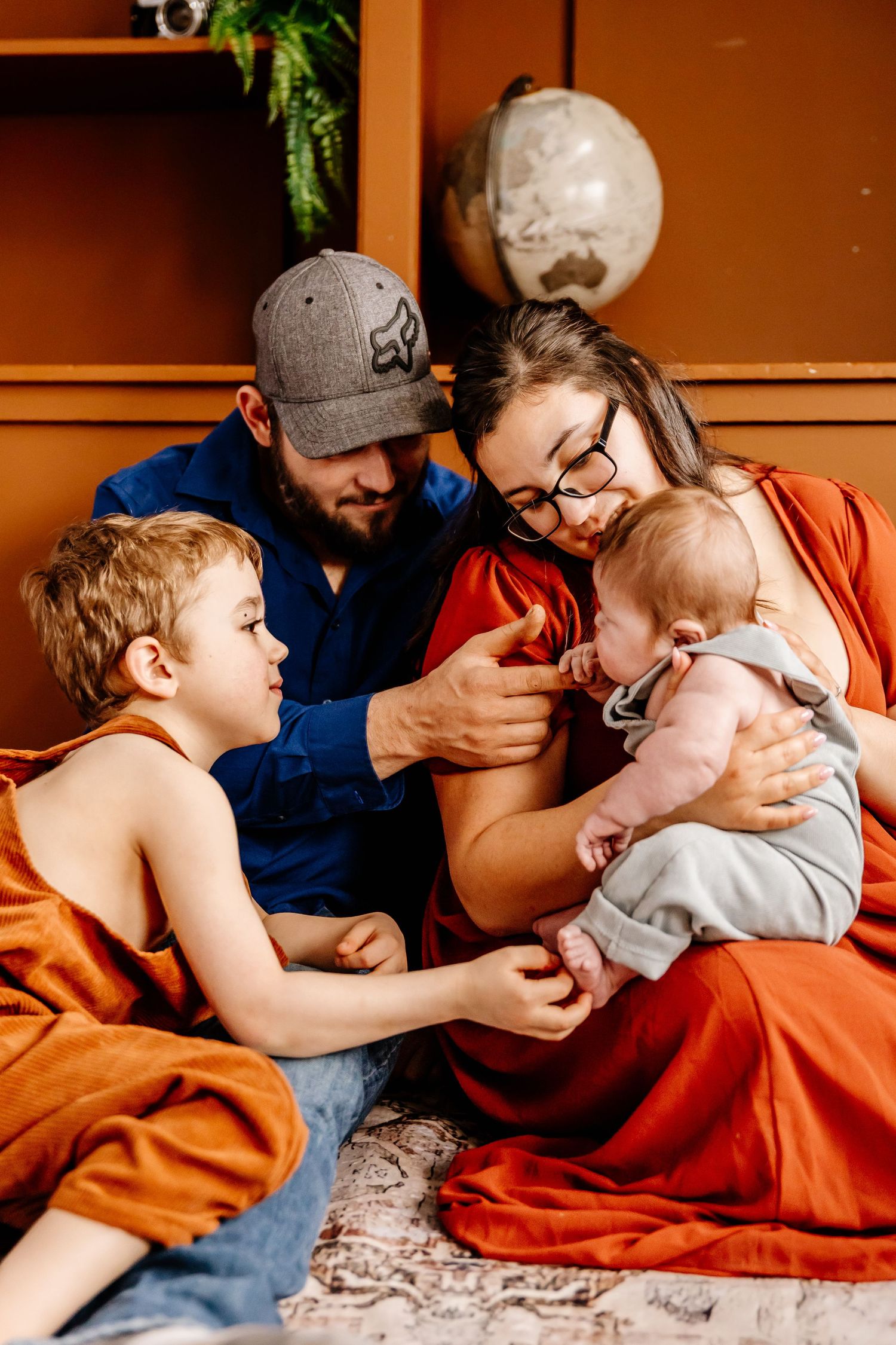 Young family of four sharing a tender moment together on the floor, with a newborn baby and toddler son.
