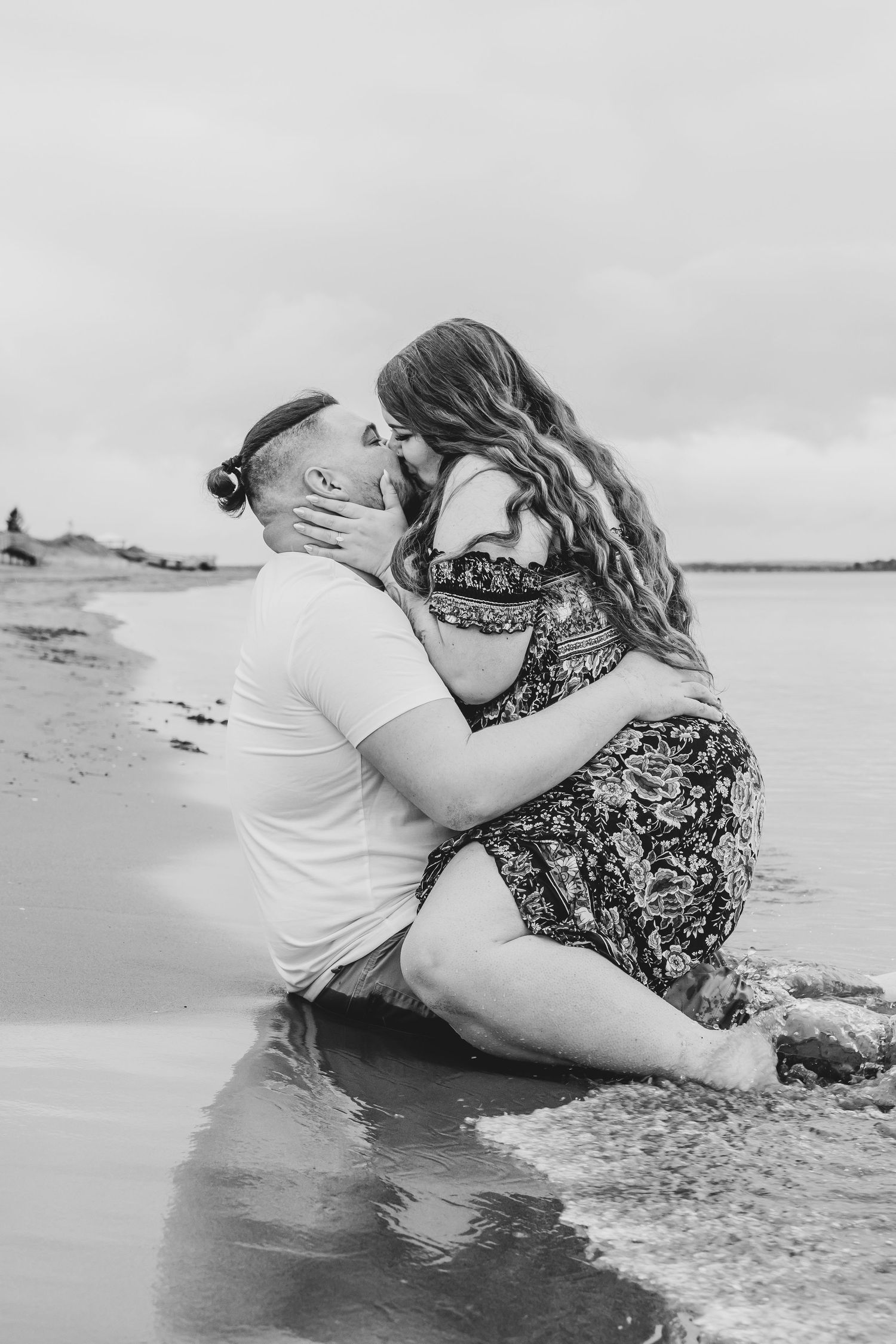 Romantic black and white photo of couple kissing on a beach shoreline.