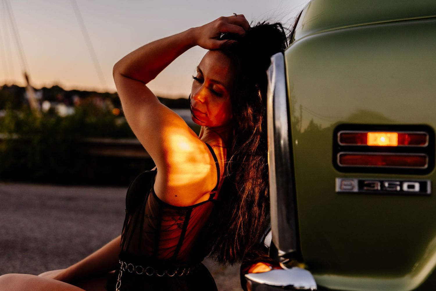 Young woman posing against a vintage green Ford F-350 truck at golden sunset hour.