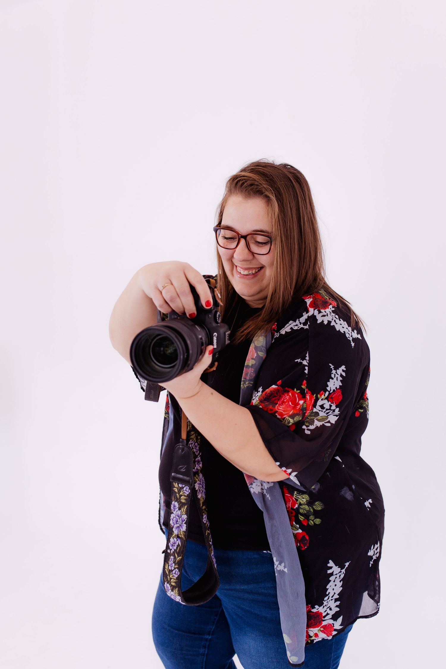 Thalie photography Female photographer in floral kimono smiling while reviewing photos on DSLR camera against white background.