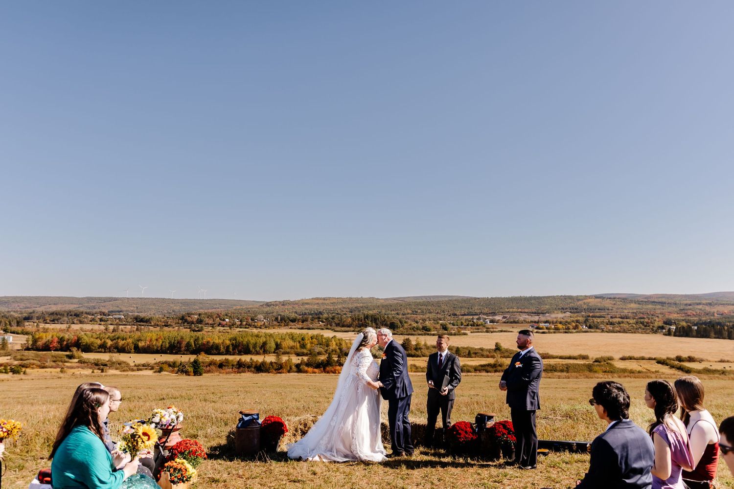 Outdoor wedding ceremony on a scenic hilltop with sweeping autumn valley views under a clear blue sky.