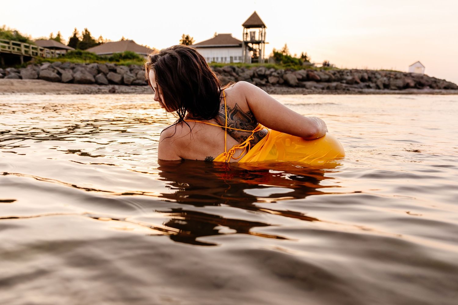 Woman in yellow swimsuit relaxing in calm ocean water at golden sunset. Bouctouche