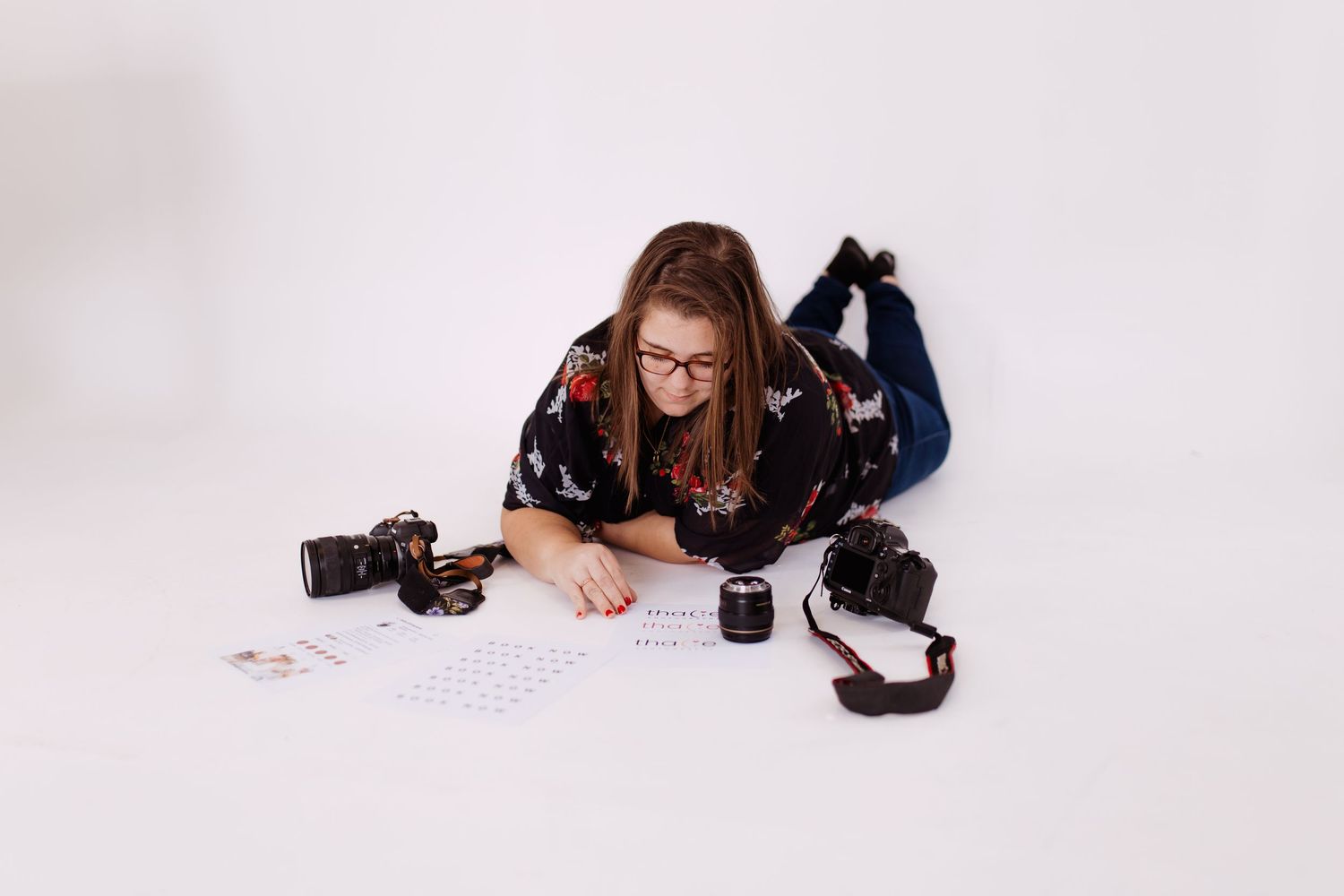 Thalie photography Female photographer lying on white floor surrounded by cameras and contact sheets.