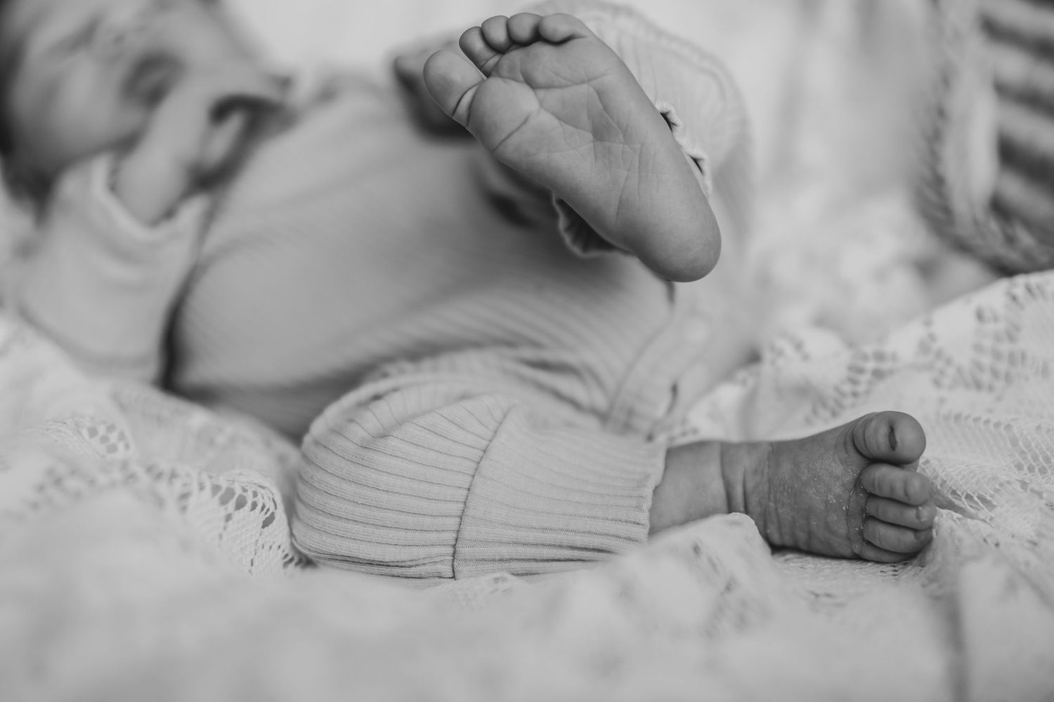Black and white close-up of newborn baby feet and tiny hands resting on soft blanket. Dieppe