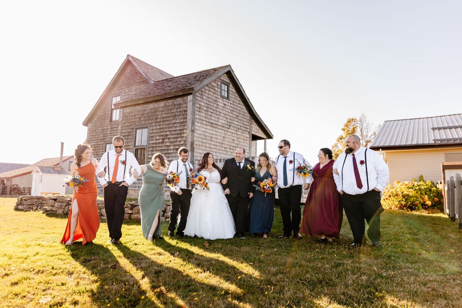 Wedding party celebrating outdoors near a rustic barn on a sunny day with colorful attire.