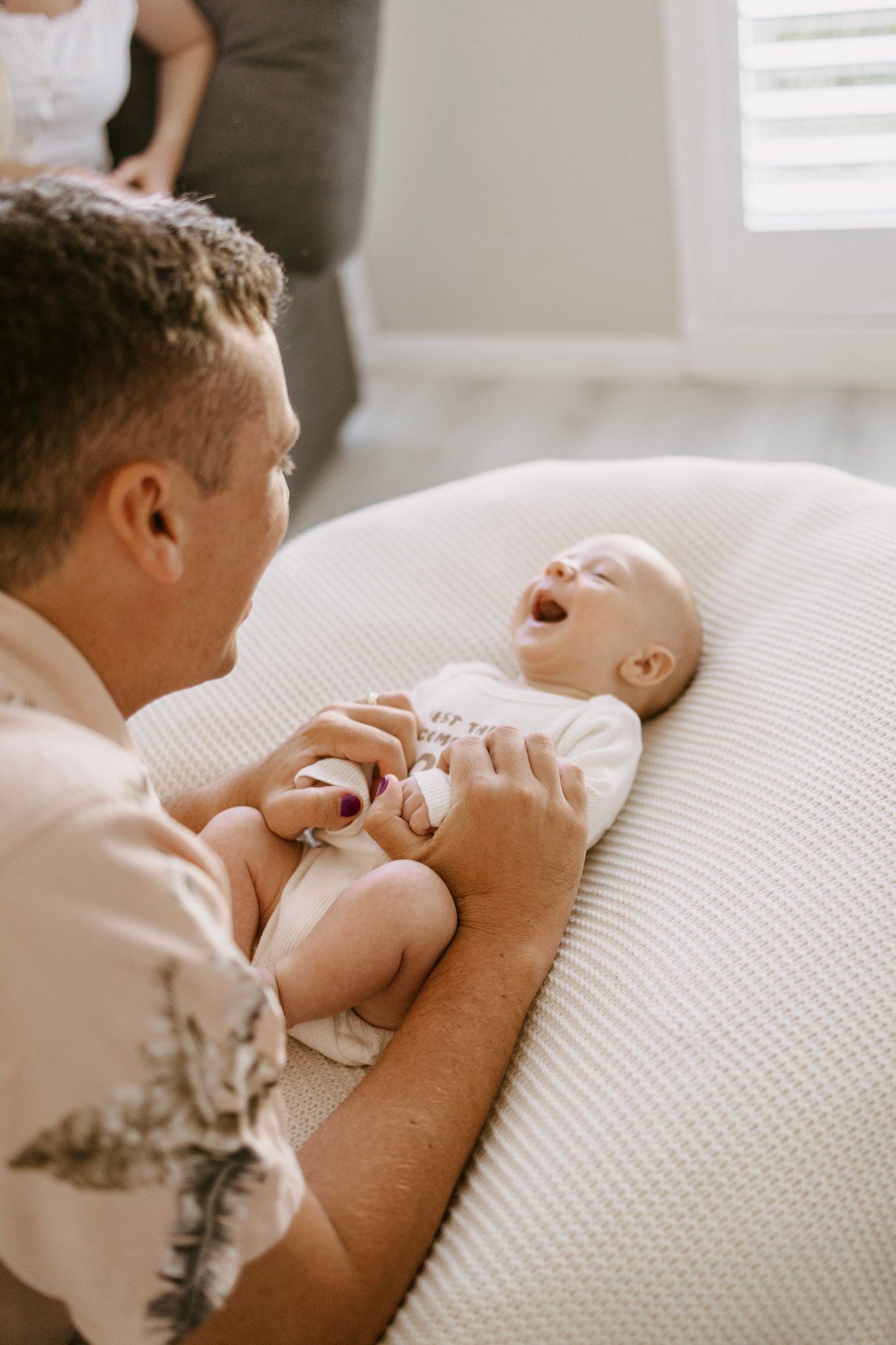 Father tenderly interacting with laughing newborn baby lying on soft cushion during indoor family photo session.