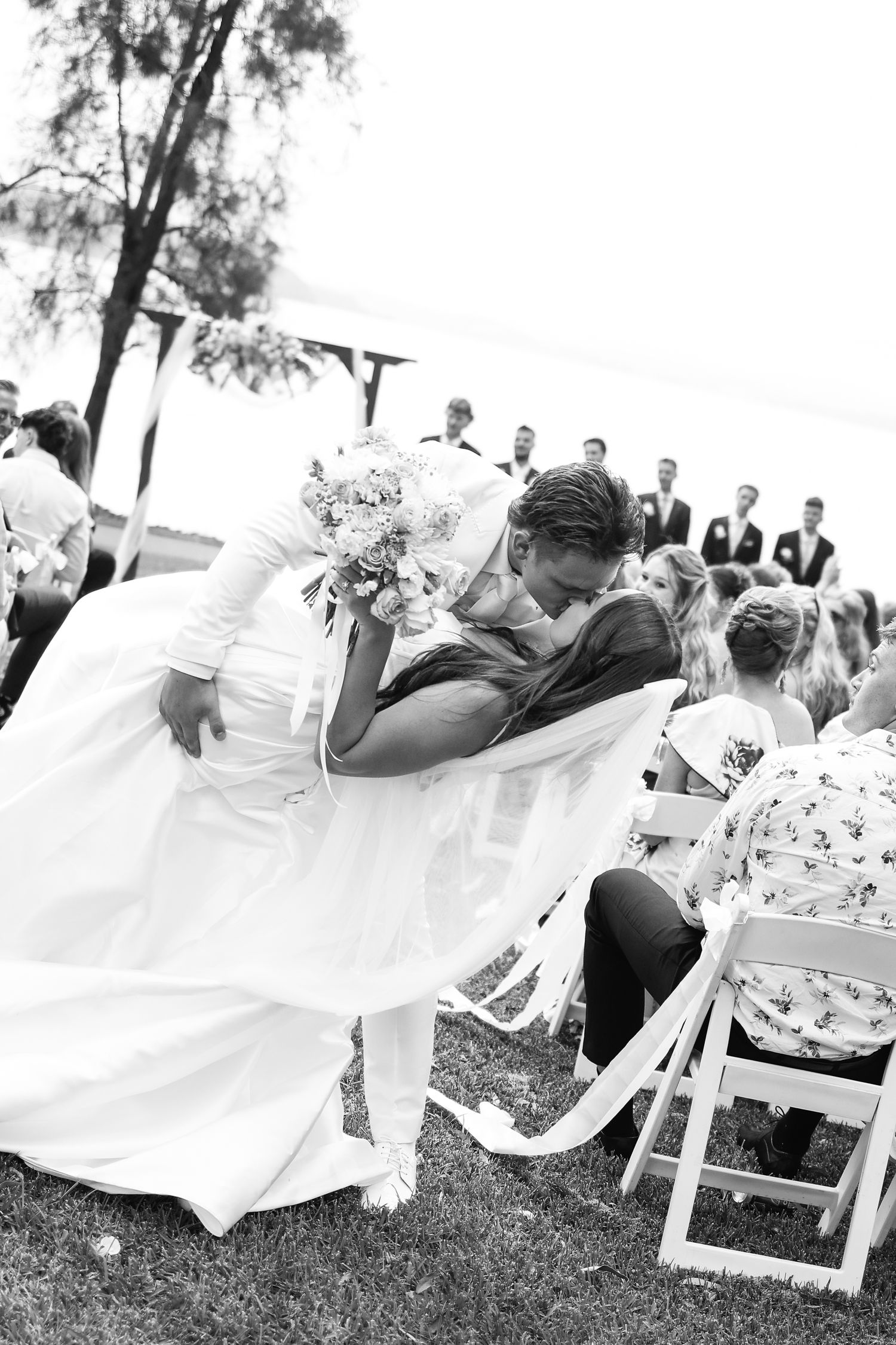 Groom dipping bride for a kiss during outdoor wedding ceremony in black and white photo.