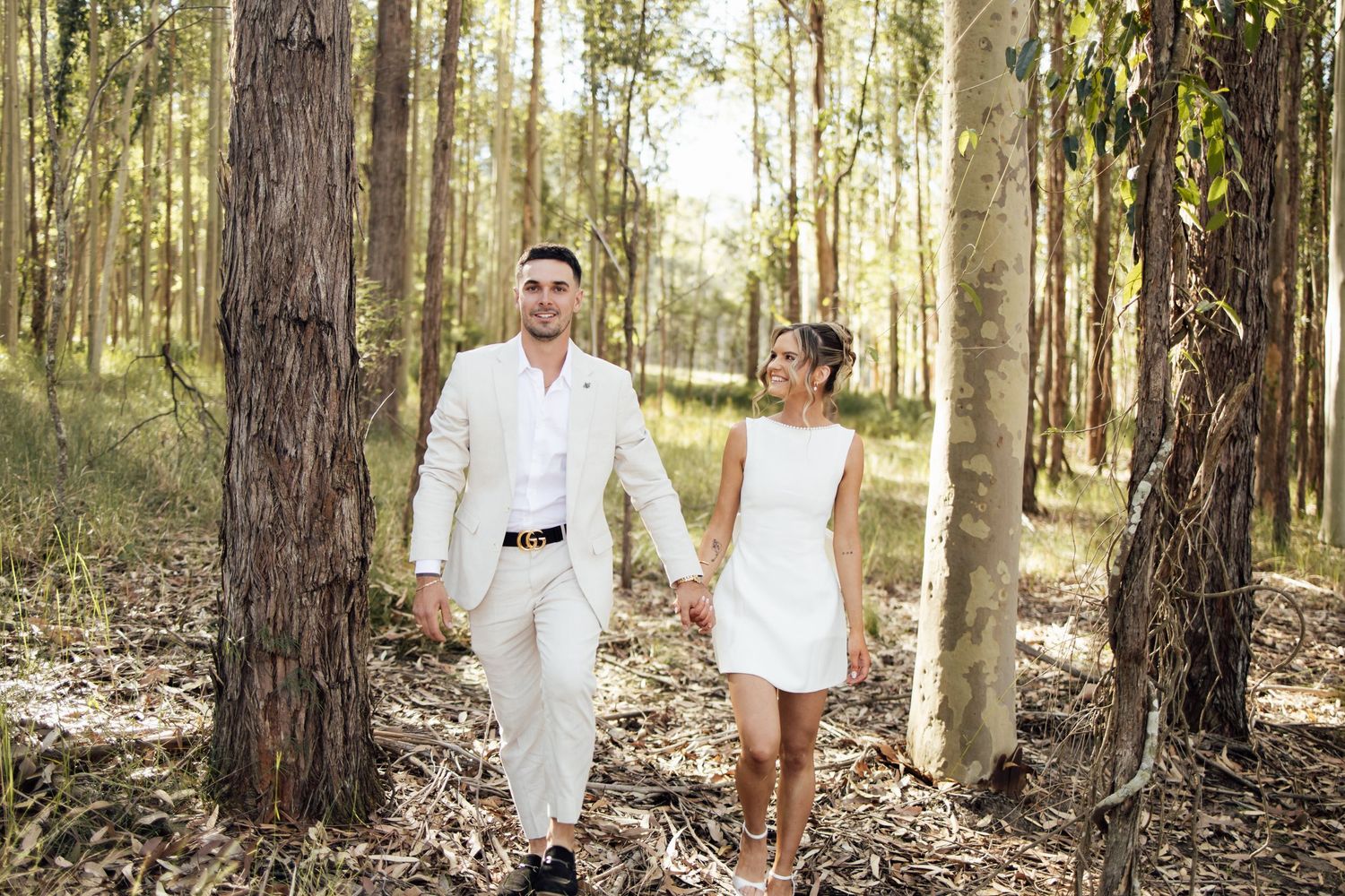 Engaged couple holding hands and walking through a beautiful sunlit eucalyptus forest.