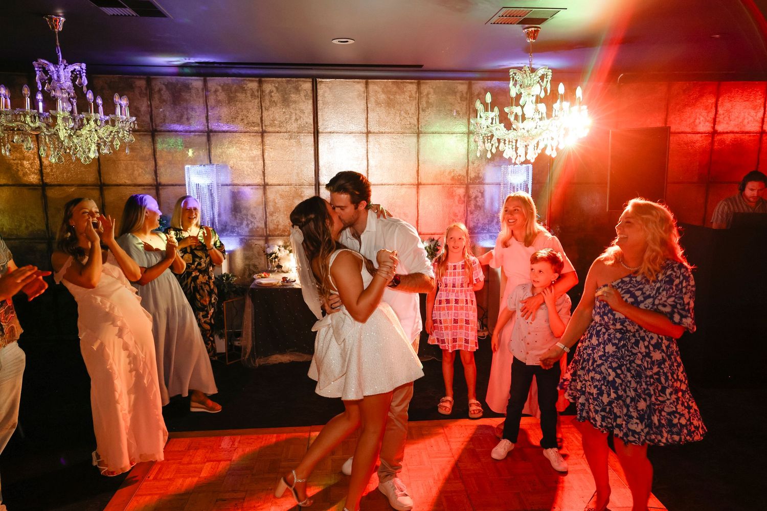 Couple sharing a romantic dance at a wedding reception with guests watching under chandelier lighting.