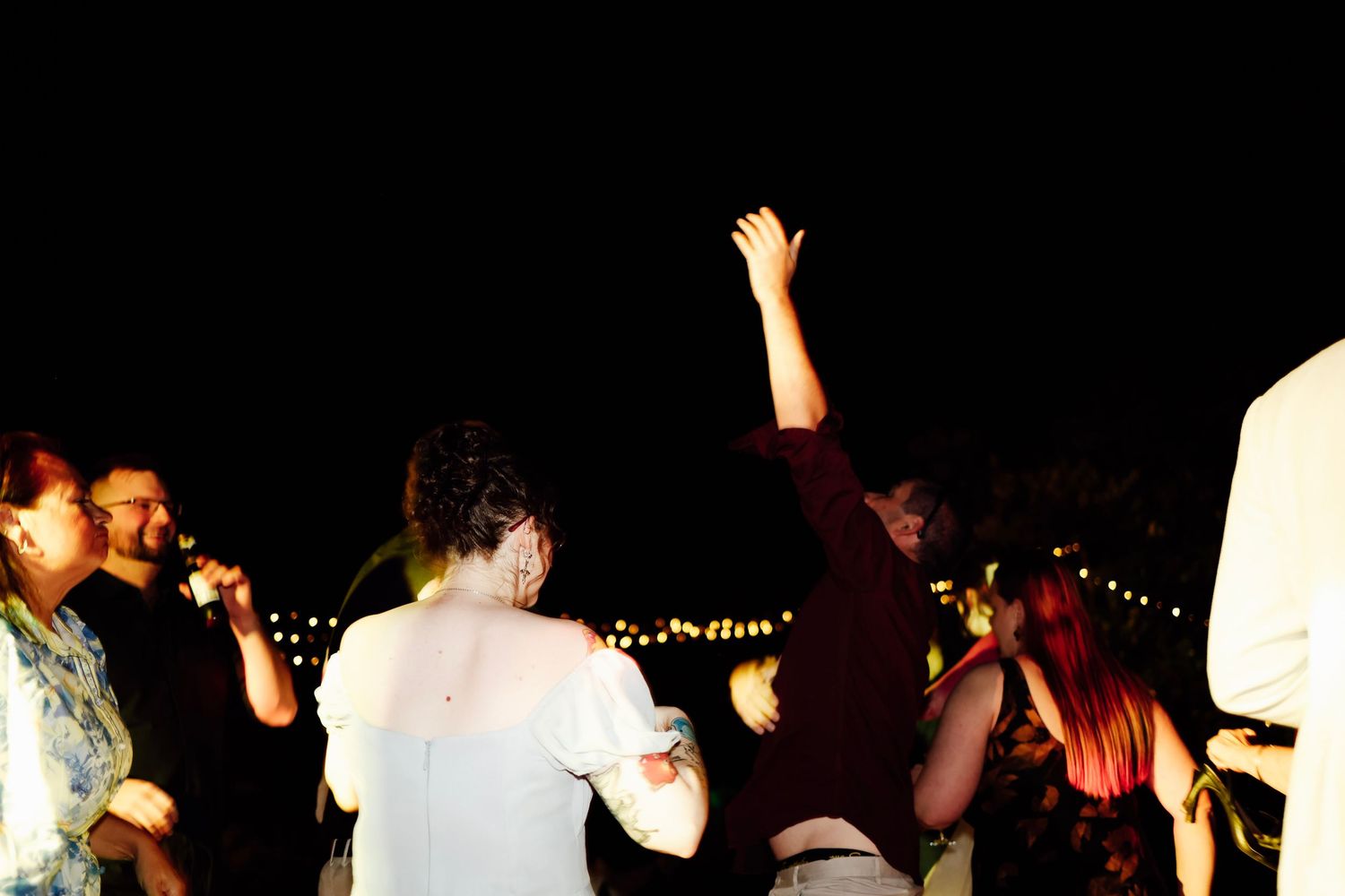 Guests dancing outdoors at night under string lights at a lively wedding reception.