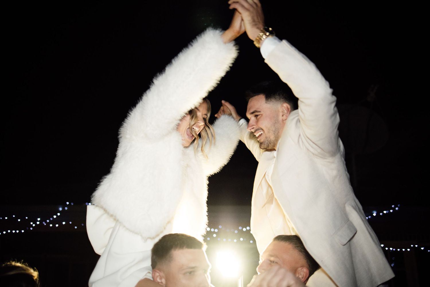 Joyful couple in white holding hands raised up high at their engagement party.