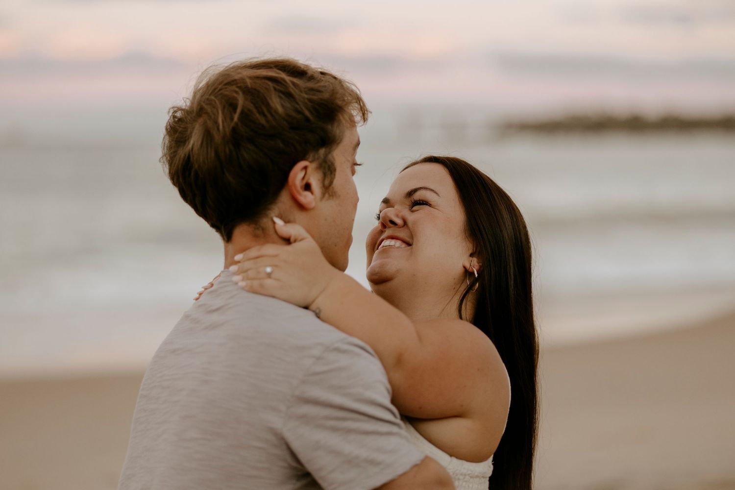 Couple sharing a tender embrace on a beach at sunset with ocean waves in background.